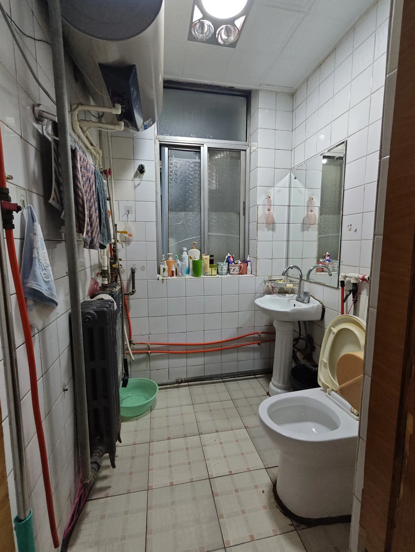 卫生间空间狭小，白色马桶、洗手台和浴缸简洁明快。台面和房间内散落着几瓶瓶物。窗户的采光让空间显得明亮。关键字:小卫生间 白色设施 瓶子 采光