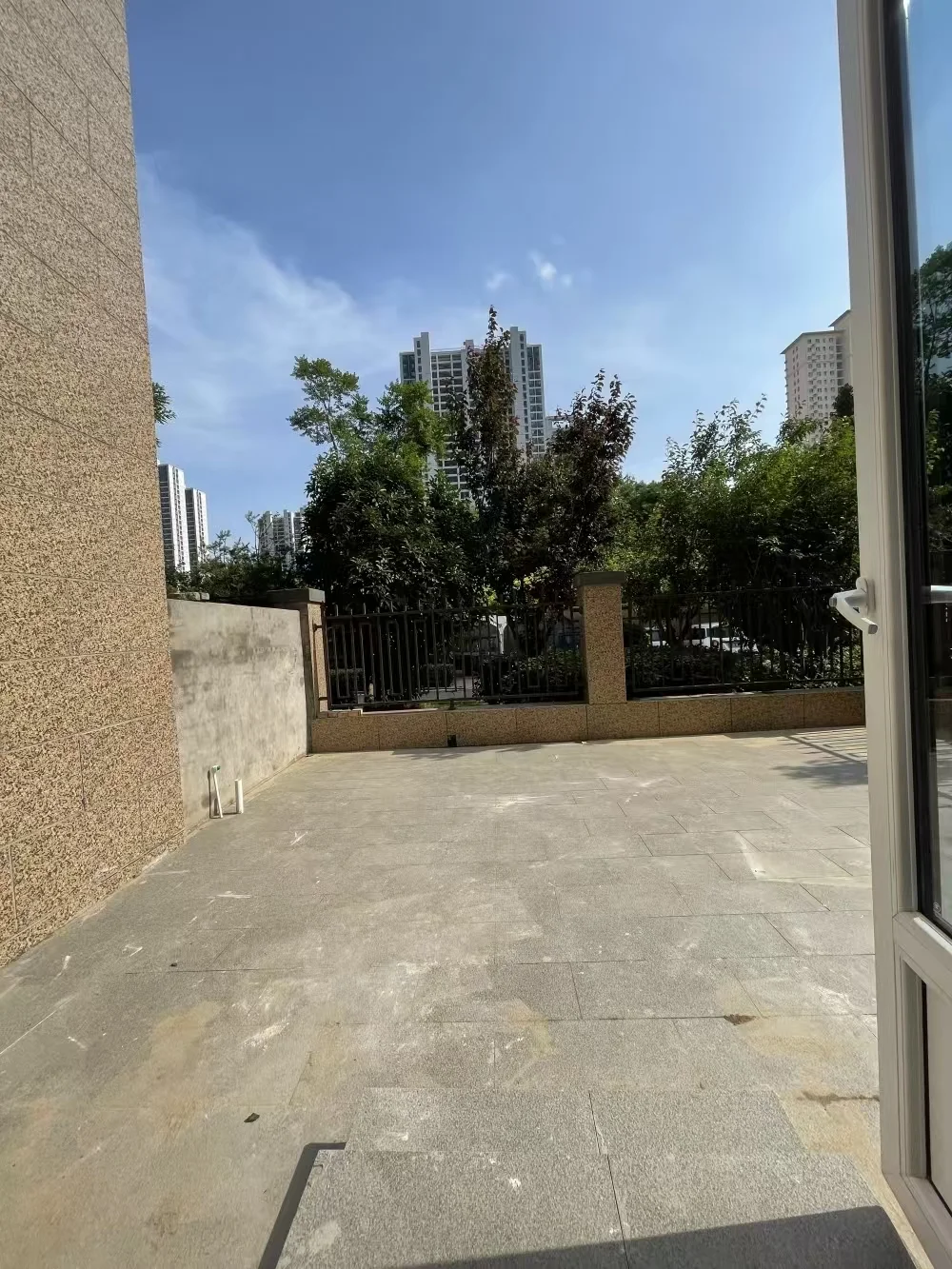 图片展示了一个大型开放庭院，周围有混凝土地板和金属围栏。庭院位于城市中，背景可见高楼。整体氛围平静，庭院是唯一可见的户外空间，无人员或其他物体。关键字:开放庭院、混凝土地板、金属围栏、城市、高楼、平静、无人员、无其他物体