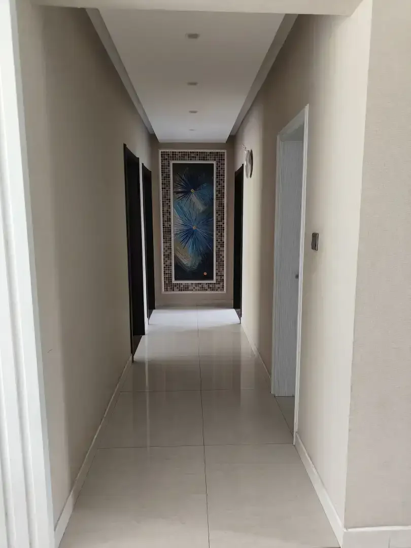 白色墙面，瓷砖地面的走廊，墙上挂着一幅画增添装饰。一端的门通向另一个房间，整体氛围干净整洁。关键字:白色墙面 瓷砖地面 走廊 装饰画 门