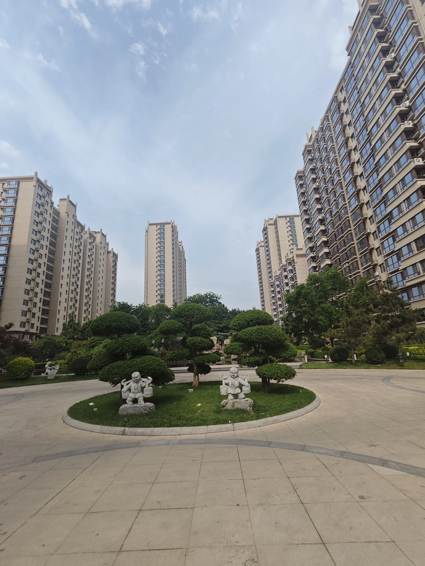 宽敞的城市广场，被高耸的现代建筑环绕，宁静而优雅。圆形设计增添视觉美感，绿树点缀其间，带来自然元素。整体氛围宁静有序，彰显都市中的宁静角落。