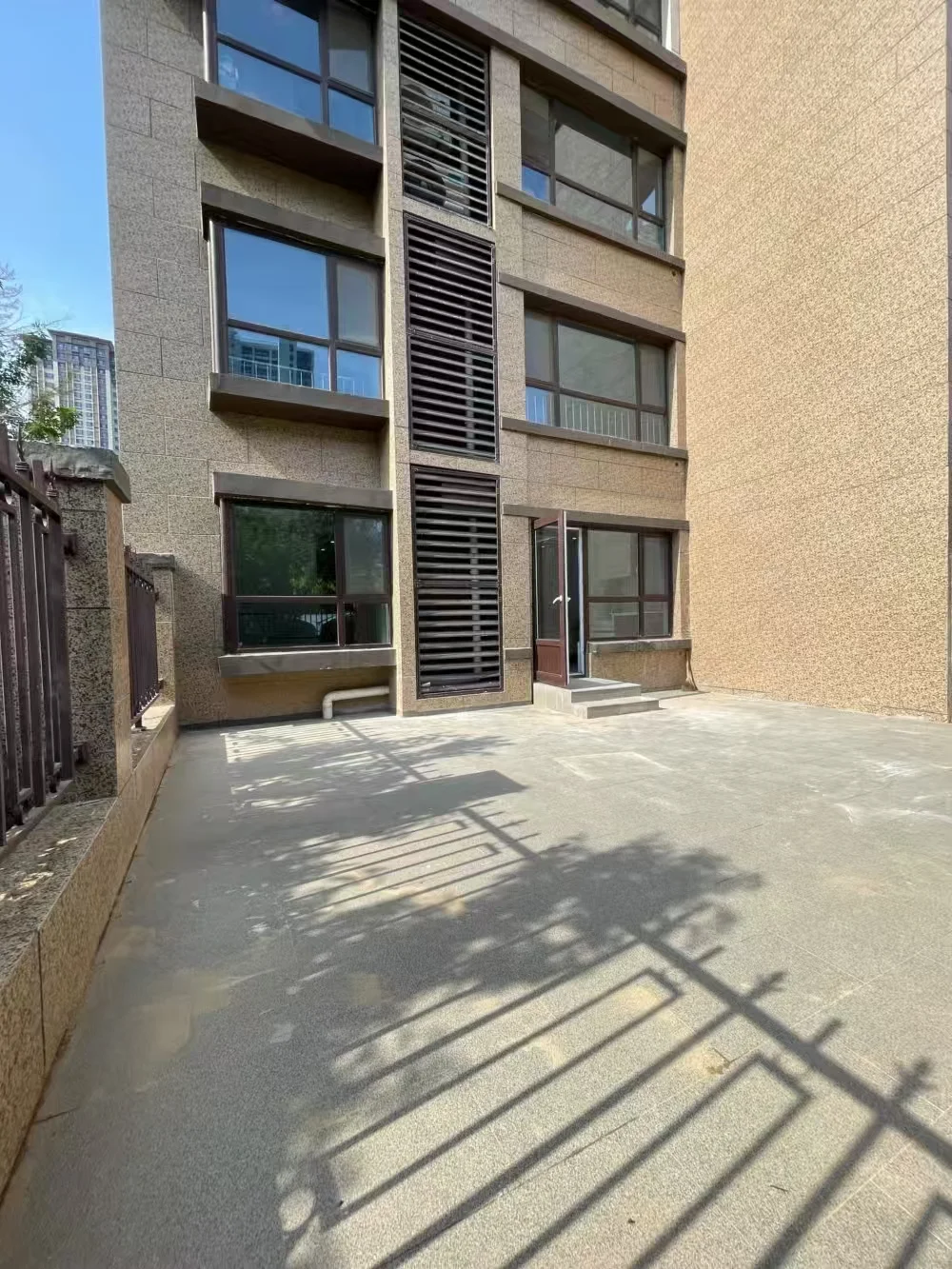 图片展示了一栋高层建筑，棕色的立面设有二楼阳台，位于城市中，周围有其他建筑，背景有树木，营造出都市生活氛围。关键字:多层建筑、棕色立面、阳台、城市环境、周围建筑、树木