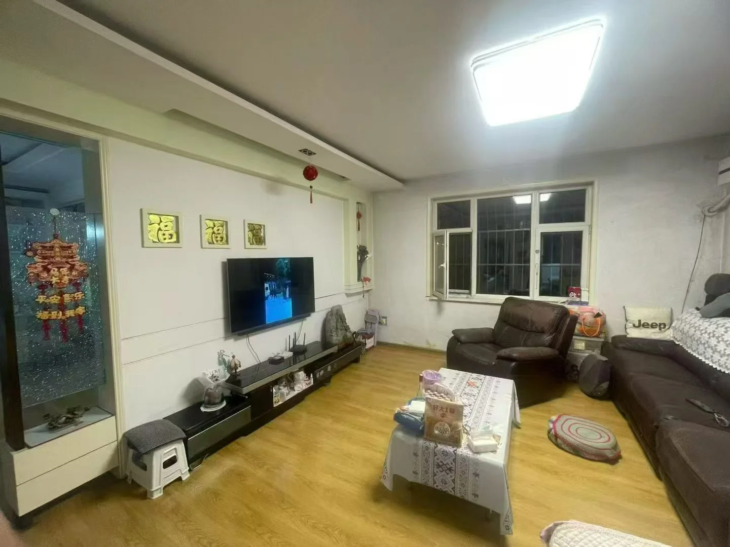 画面是一个客厅，墙上挂着一台平板电视。房间氛围温馨，沙发和椅子靠近电视。房间里还有一张餐桌，增加了空间的实用性。客厅看起来井井有条且干净，整齐排列着一些物品，包括一盆植物、一个花瓶和一本书。这些物品的存在表明房间主要用于休闲和娱乐。关键字:客厅,平板电视,沙发,椅子,餐桌,植物,花瓶,书