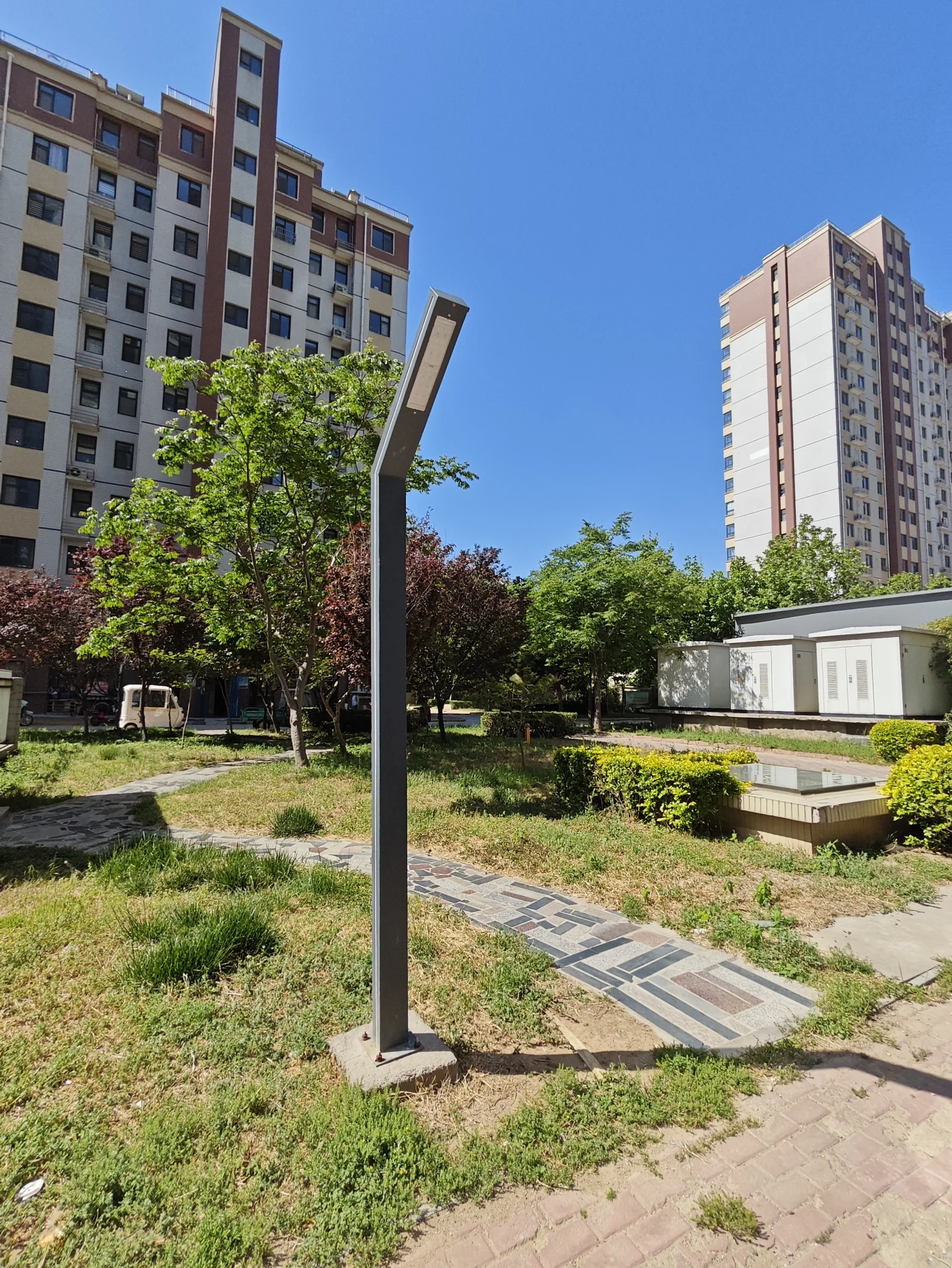 公园有人行道和草地区域，街灯立在人行道上，背景中有一栋高楼。公园看起来空无一人，没有其他物体。气氛显得平静而宁静，公园中的自然元素和街灯营造出一个宁静的环境。