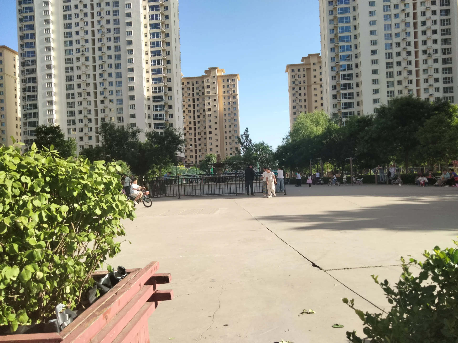 开阔空间，现代建筑，绿树成荫，休闲氛围浓厚，行人悠闲，车辆停放繁忙，展现都市生活与自然和谐共处的美好。关键字:开阔空间 现代建筑 绿树成荫 休闲氛围 行人悠闲 车辆停放繁忙 都市生活