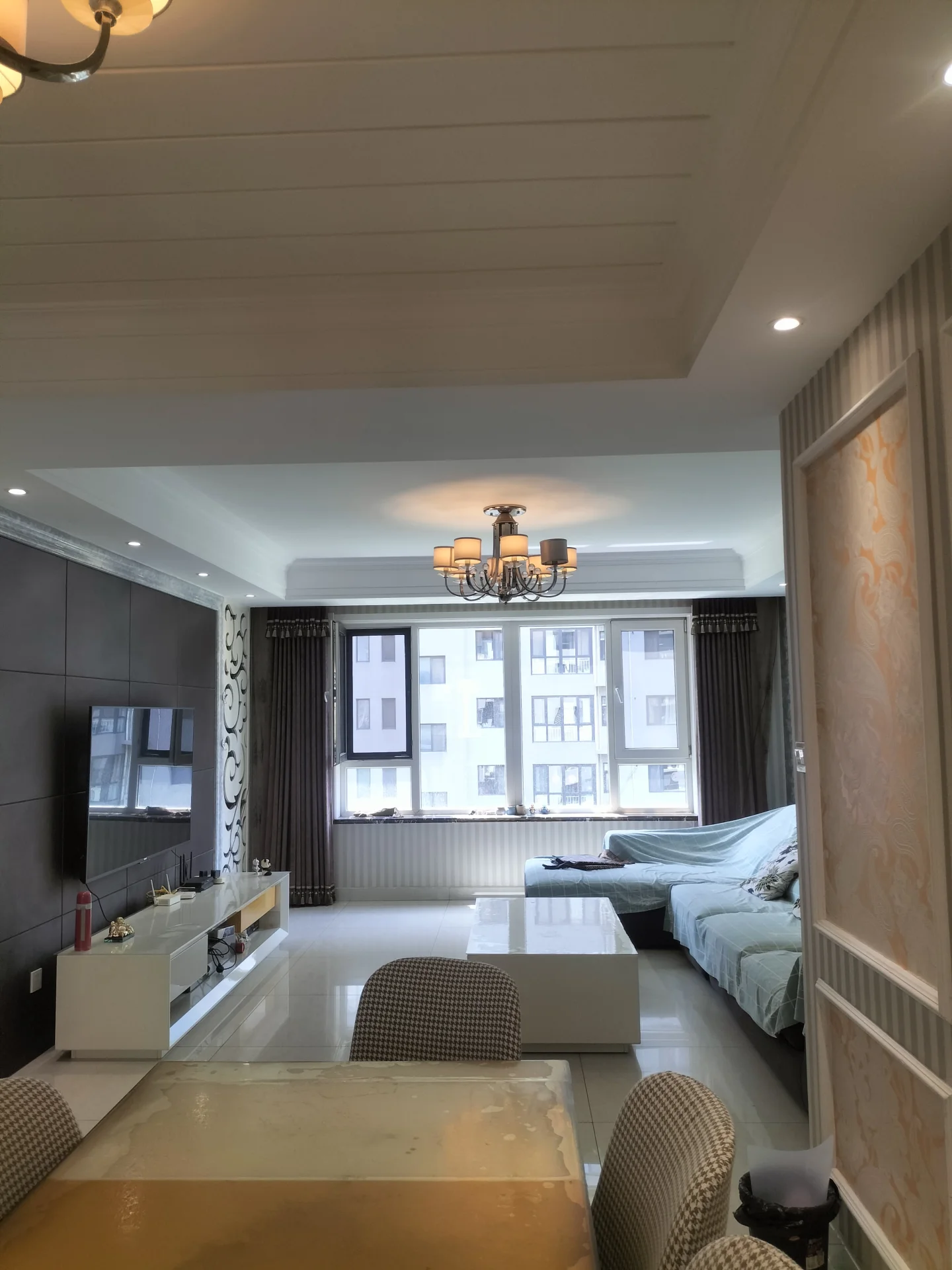 宽敞明亮客厅，大窗让自然光充盈空间，餐桌椅围绕，沙发和电视，家具布置温馨舒适，增添氛围的有花瓶、酒瓶和书籍，传达放松休闲的感觉，客厅作为家人朋友聚会中心。