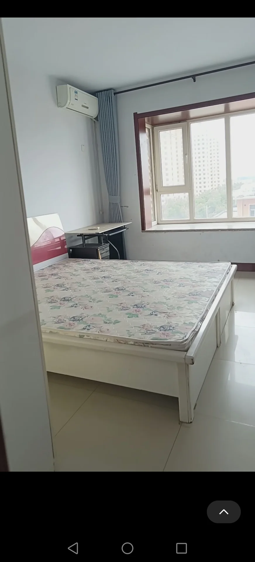 图片展示了一个白色床和一个窗户的卧室。房间看起来干净整洁，床靠墙摆放，旁边还有一张书桌。气氛显得平静祥和，窗户提供自然光照给空间。房间内的物品包括一张床、一张书桌和一扇窗户，创造了一个功能性舒适的居住区域。