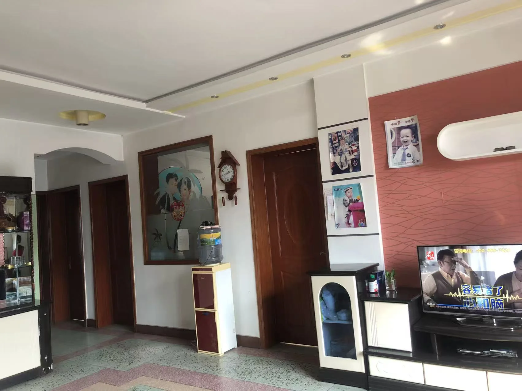 图片展示的是一个有电视、钟表和花瓶的客厅。房间氛围温馨，墙上挂着钟表，桌上摆放着花瓶。客厅看起来是一个小型的亲密空间，可能是工作室公寓的一部分。电视的存在表明这是一个用于放松和娱乐的空间。整体环境给人一种舒适且宜人的居住氛围。关键字:客厅,电视,钟表,花瓶,工作室公寓