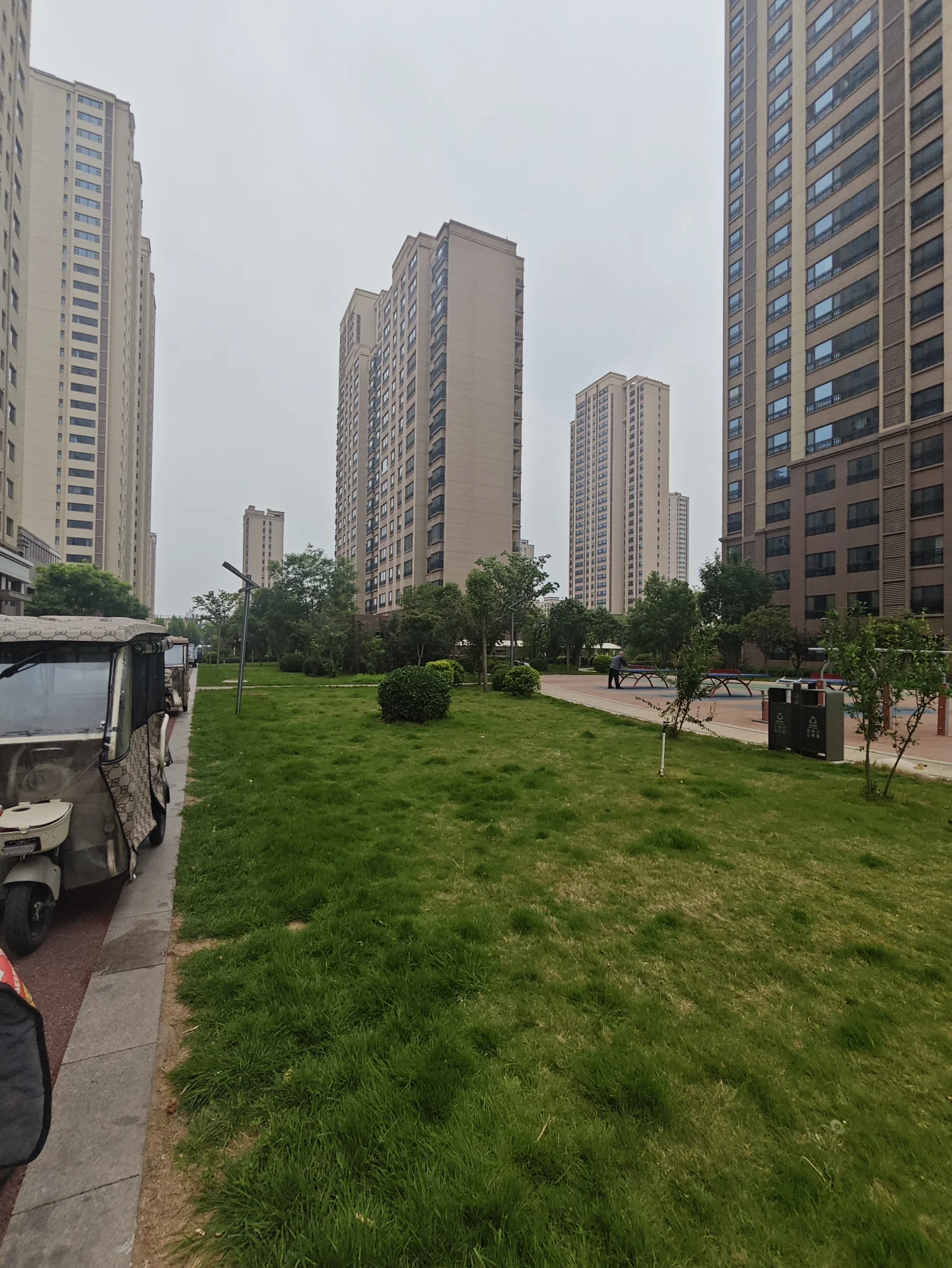 城市街道，高楼林立，路边停有汽车和卡车，行人走在人行道上，建筑风格为高层公寓或 condos。
