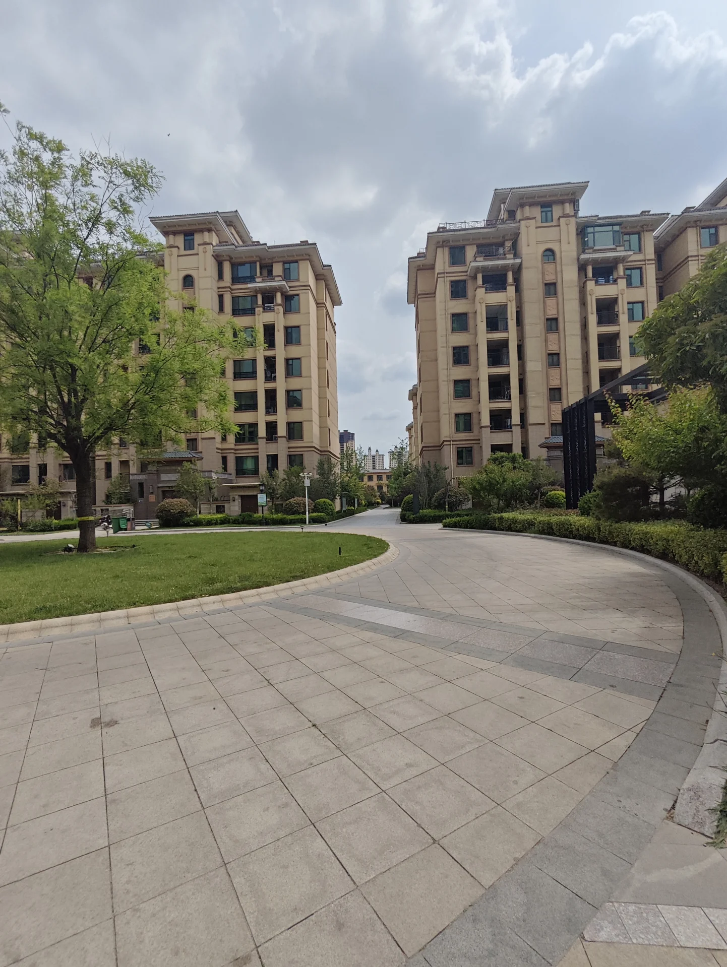 宽阔的城市街道两侧，高耸的现代建筑整齐排列，天空阴沉，营造出一种宁静而略显压抑的氛围。街道上行人稀少，车辆不多，偶尔有几辆汽车停在路边。沿人行道摆放的长椅为路人提供了休息的地方。关键字:城市街道 高耸建筑 阴沉天气 现代建筑 宁静氛围 稀少行人 长椅