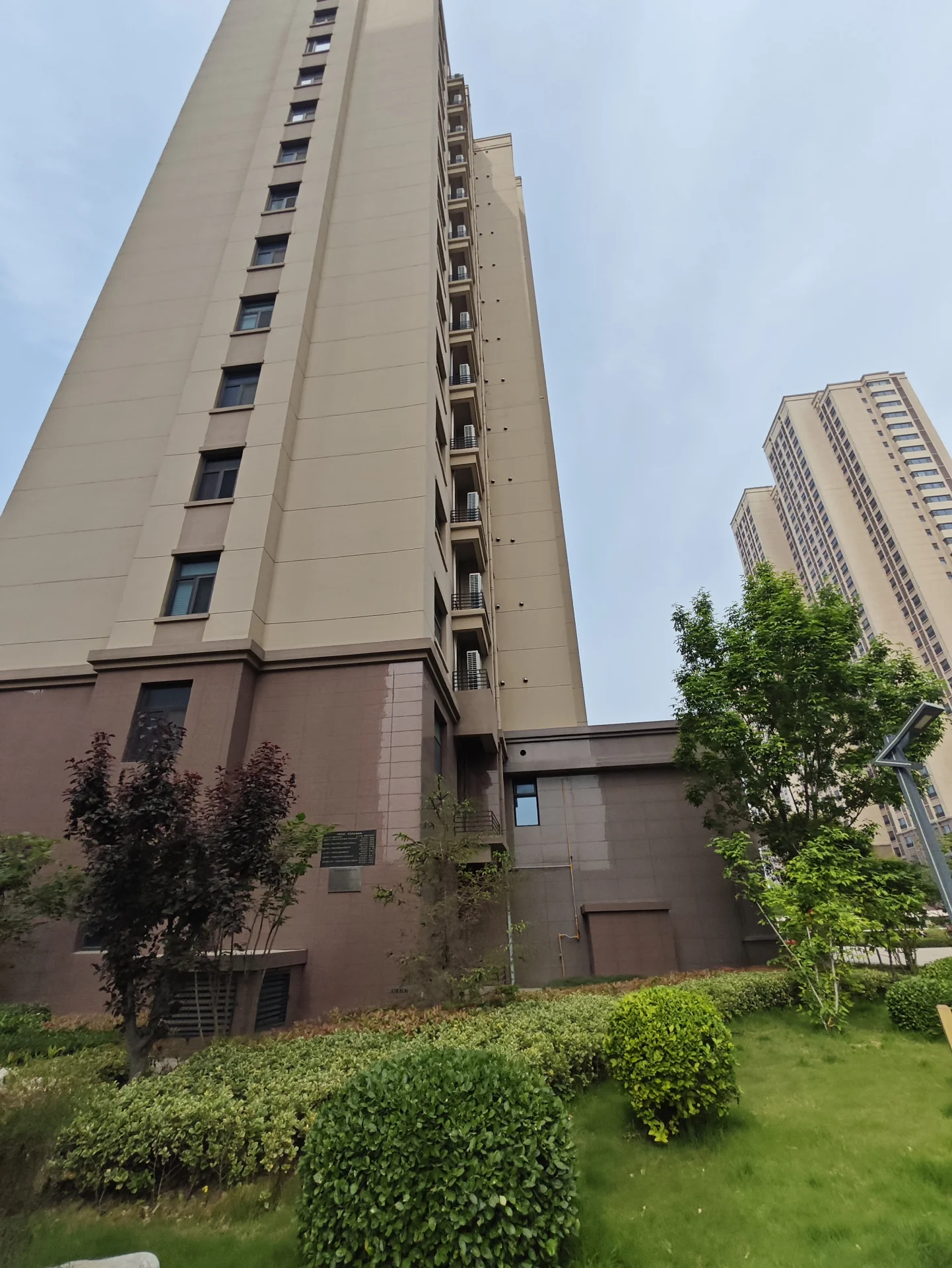 这是一栋现代风格的高层建筑，可能是办公楼或住宅区，位于树木和灌木丛前，营造出宁静舒适的氛围。建筑外观 sleek，外部空旷无人，显得较为安静或尚未繁华。关键字:现代建筑 高层楼 办公楼 住宅区 树木 灌木丛 宁静氛围 sleek外观