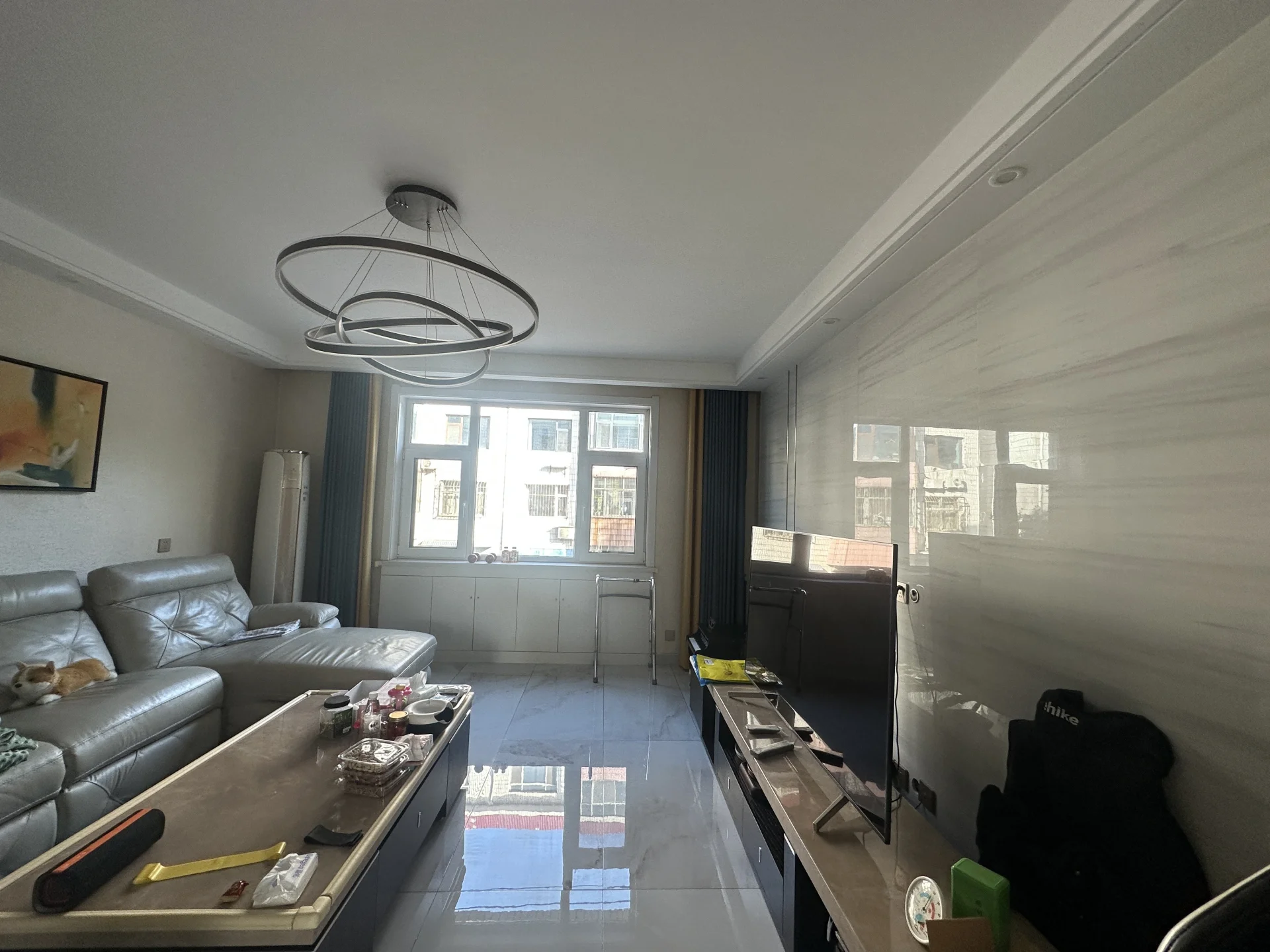 客厅空间，采用深色皮革沙发和木质茶几作为主要家具，地面铺设光洁的瓷砖。房间采光适中，整体装修风格偏向实用和基础配置。