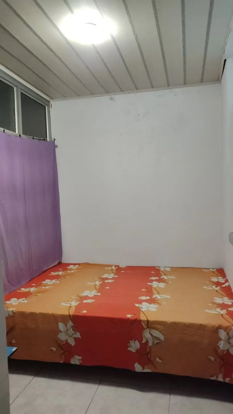 卧室空间，床铺铺设带有橙色和白色花卉图案的床单，房间内光线充足，整体环境简洁实用。