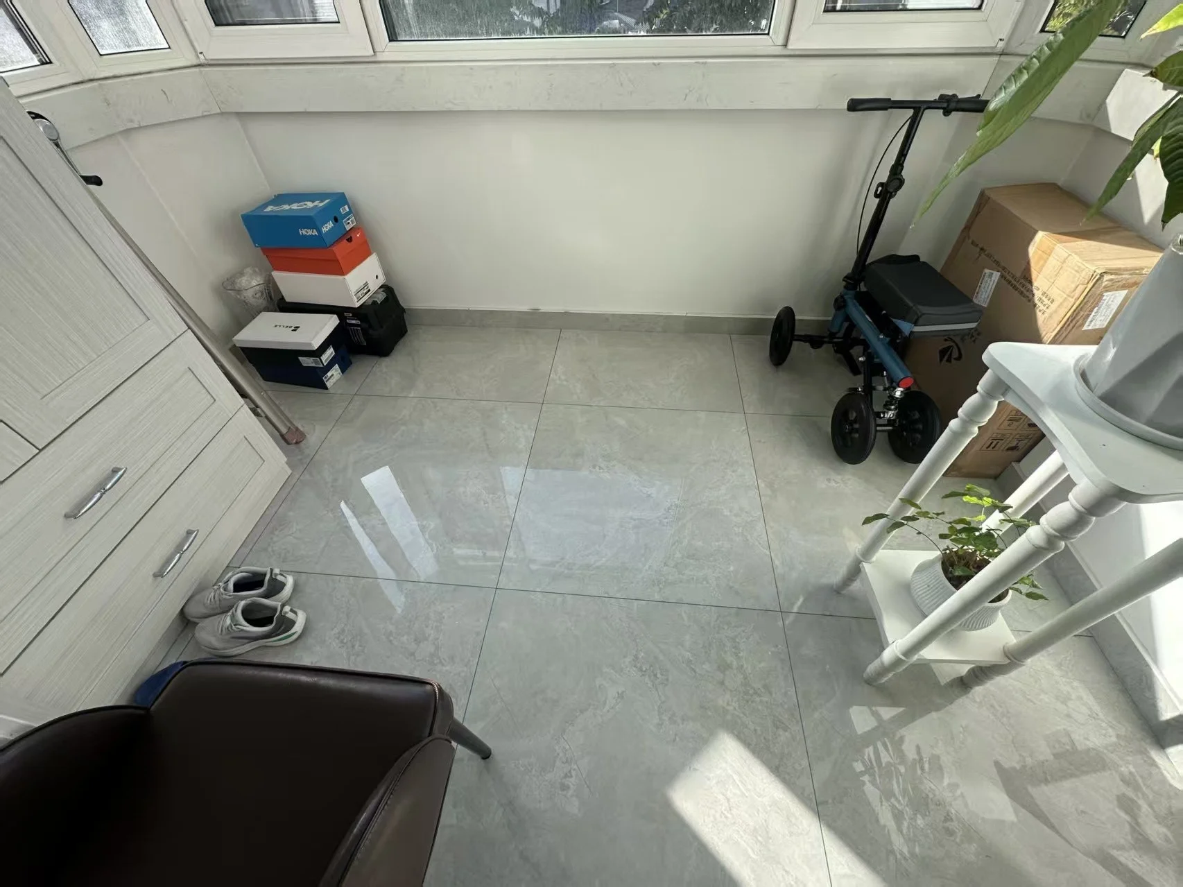 一个宽敞的室内空间，地面铺设浅色瓷砖，墙面简洁，配有一张深色皮质沙发。房间采光良好，整体呈现出装修初期或待布置的状态。