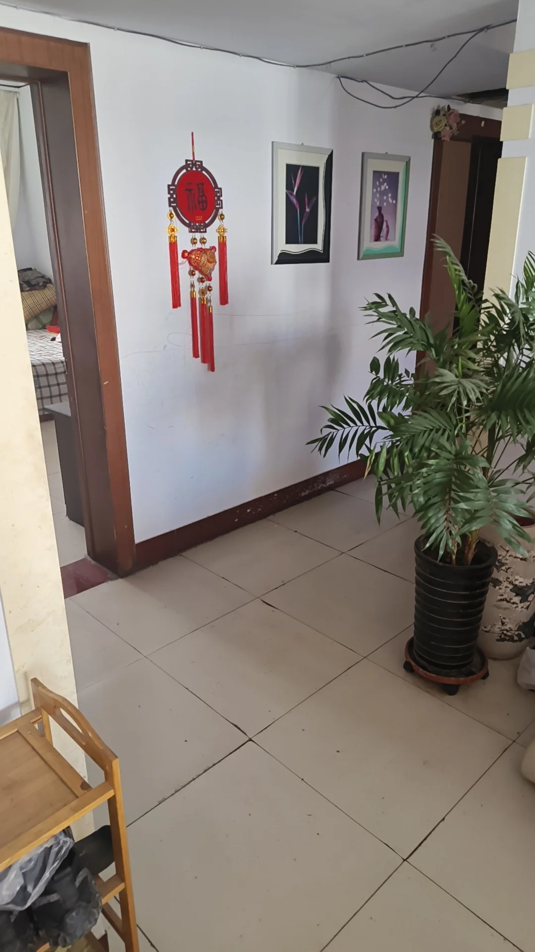 一个室内空间，地面铺设浅色瓷砖，墙面为白色，装饰有红色灯笼和几幅挂画。空间布局简洁，采光适中，整体呈现出基础的居住环境。