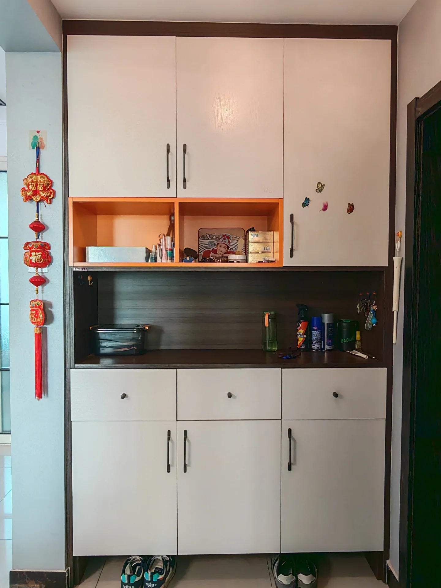 一个储物柜/衣帽间场景，柜体采用白色和深棕色木纹搭配，内部设有多个开放式和封闭式储物格。整体环境整洁，光线适中。