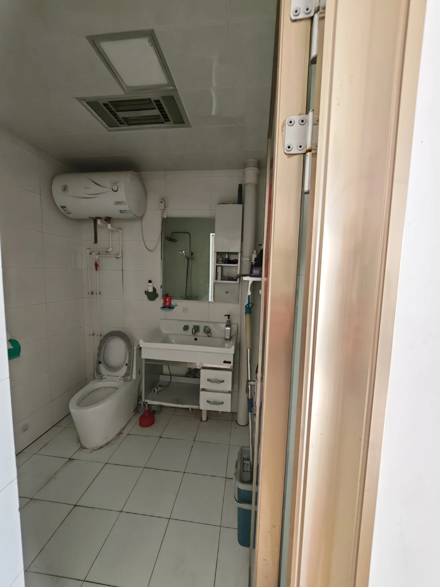 卫生间空间，墙面和地面铺设白色瓷砖，配有白色马桶、洗手台及挂壁式空调。整体装修风格简洁实用，光线明亮。