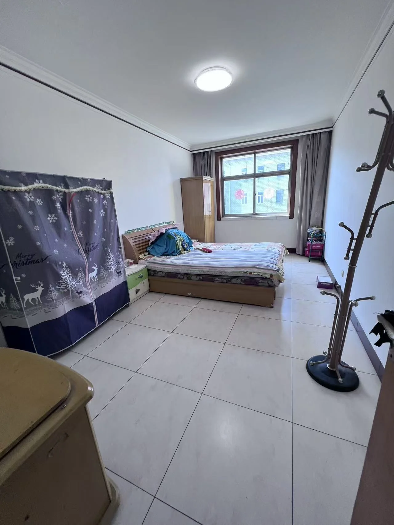 卧室空间，地面铺设浅色瓷砖，房间内摆放有床和衣柜等基础家具。采光适中，整体装修风格简洁实用。