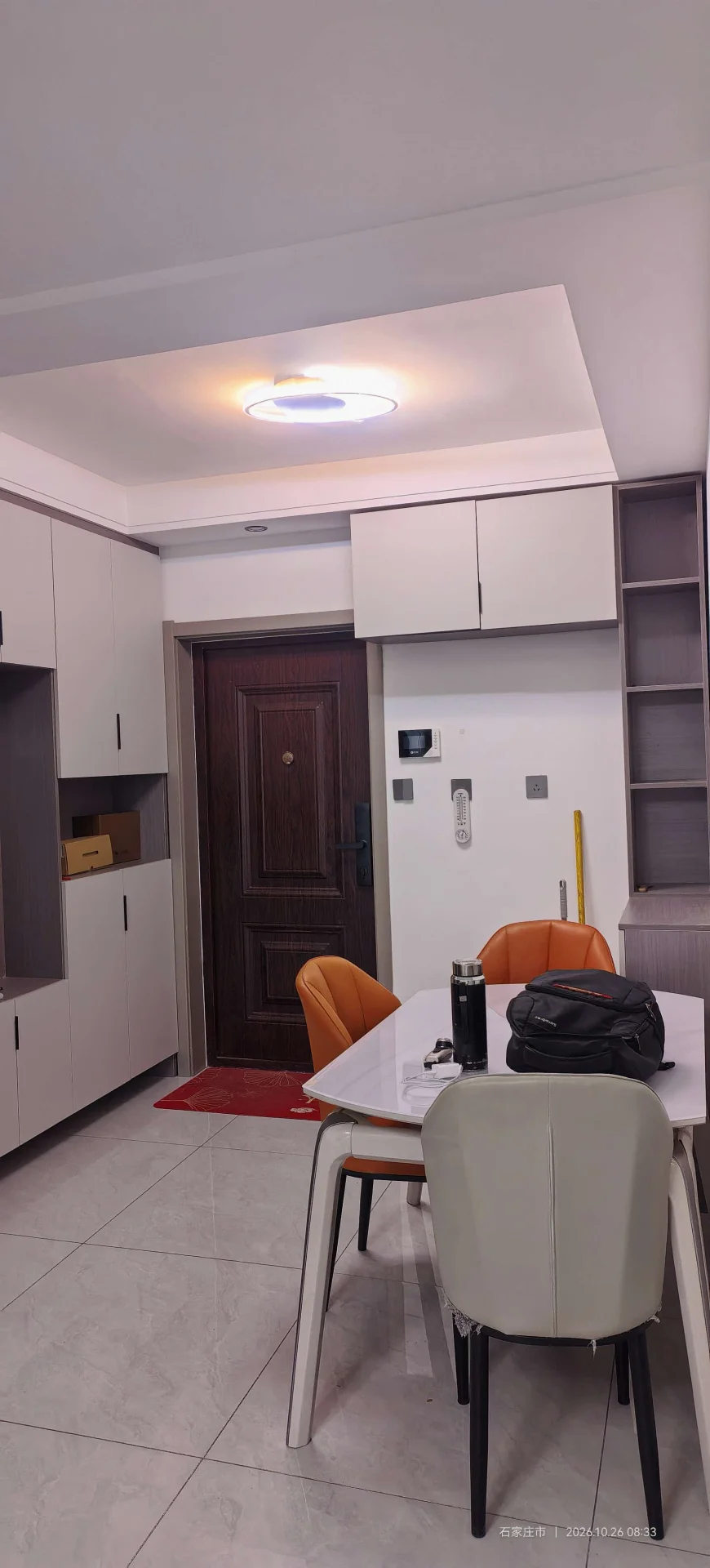 这是一个开放式厨房和餐厅区域，墙面和橱柜采用白色调，设计简洁现代。地面铺设浅色瓷砖，中央设置了餐桌及几把椅子，整体采光良好，环境整洁舒适。