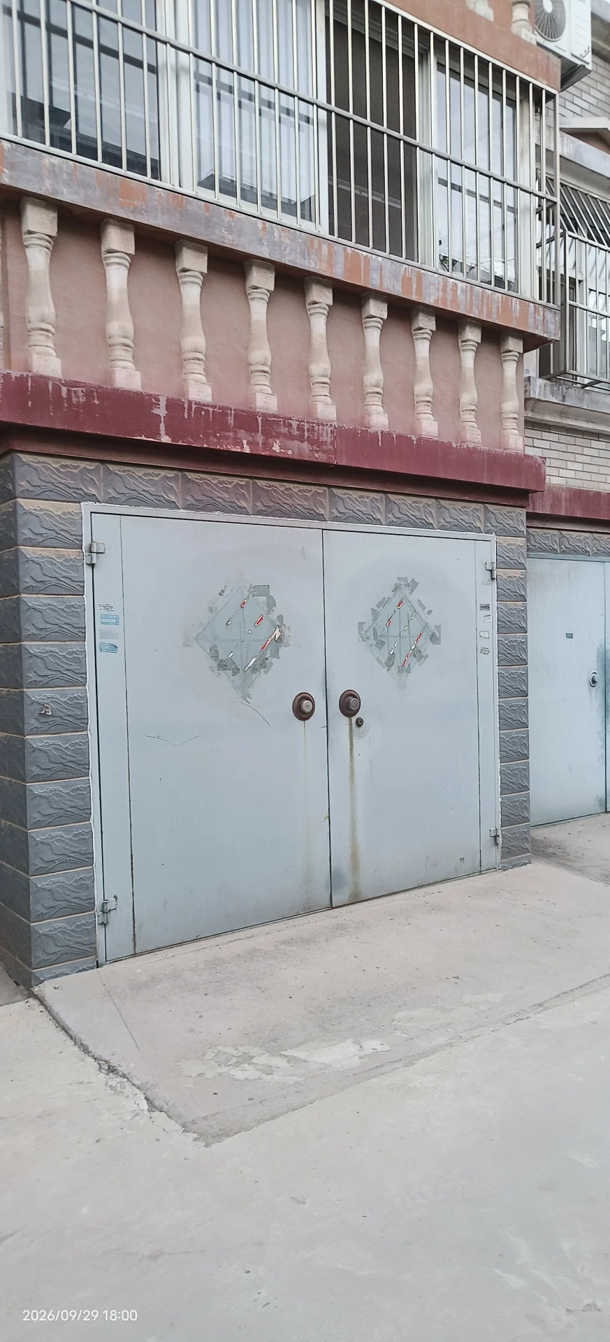 一栋多层建筑的底层，设有大型金属卷帘门作为入口，建筑外墙带有古典风格的柱式装饰。整体环境较为朴素，展现出一定的商业或工业用途。