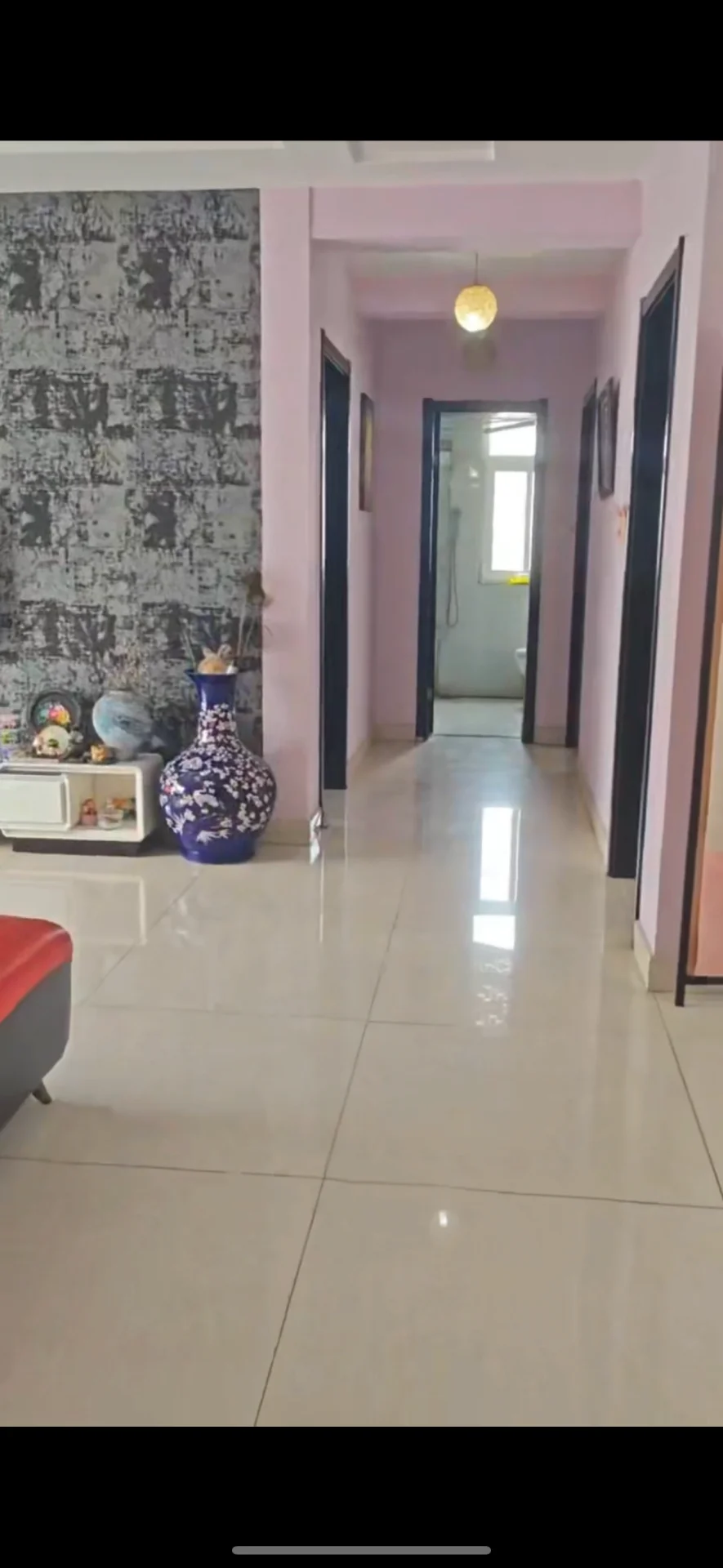 走廊空间，地面铺设大尺寸浅色瓷砖，墙面局部采用深色纹理装饰，配有简约的吊灯照明。整体环境整洁明亮，具有基础的居住功能。