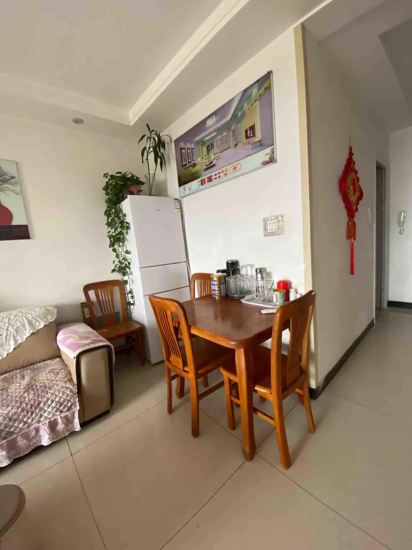 这是一个开放式居住空间，包含一个用餐区和一个休息区。用餐区设置了木质餐桌和配套椅子，旁边有一台白色冰箱。整体装修风格偏向基础实用型，采光适中。