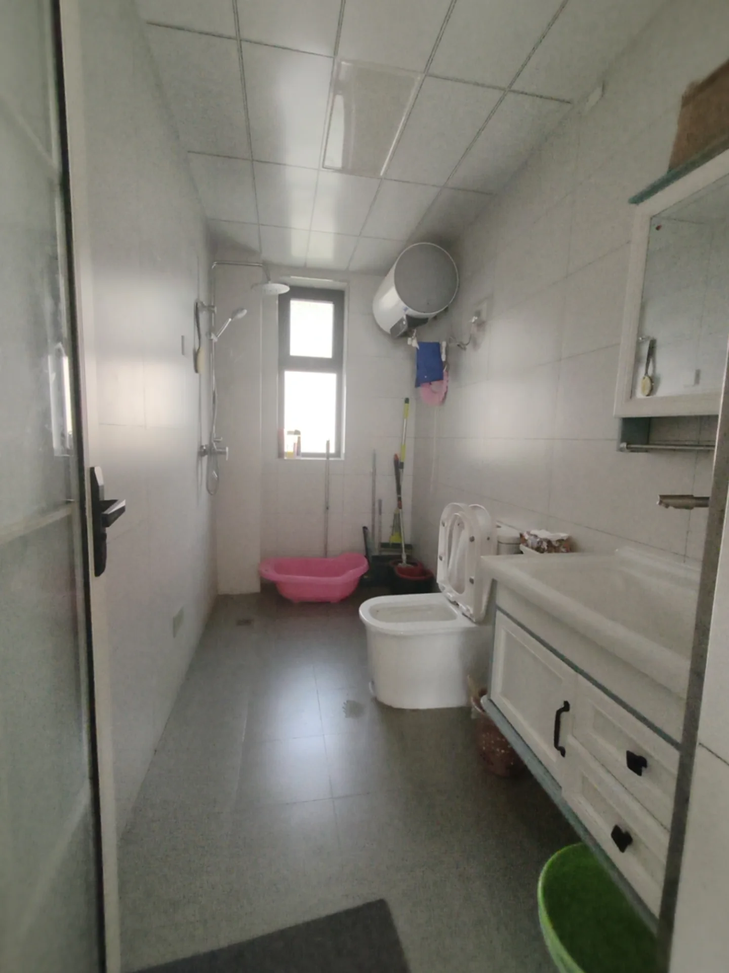 卫生间空间，墙面和地面铺设浅色瓷砖，配有白色马桶、洗手台及淋浴区。整体装修风格简洁实用，光线适中。
