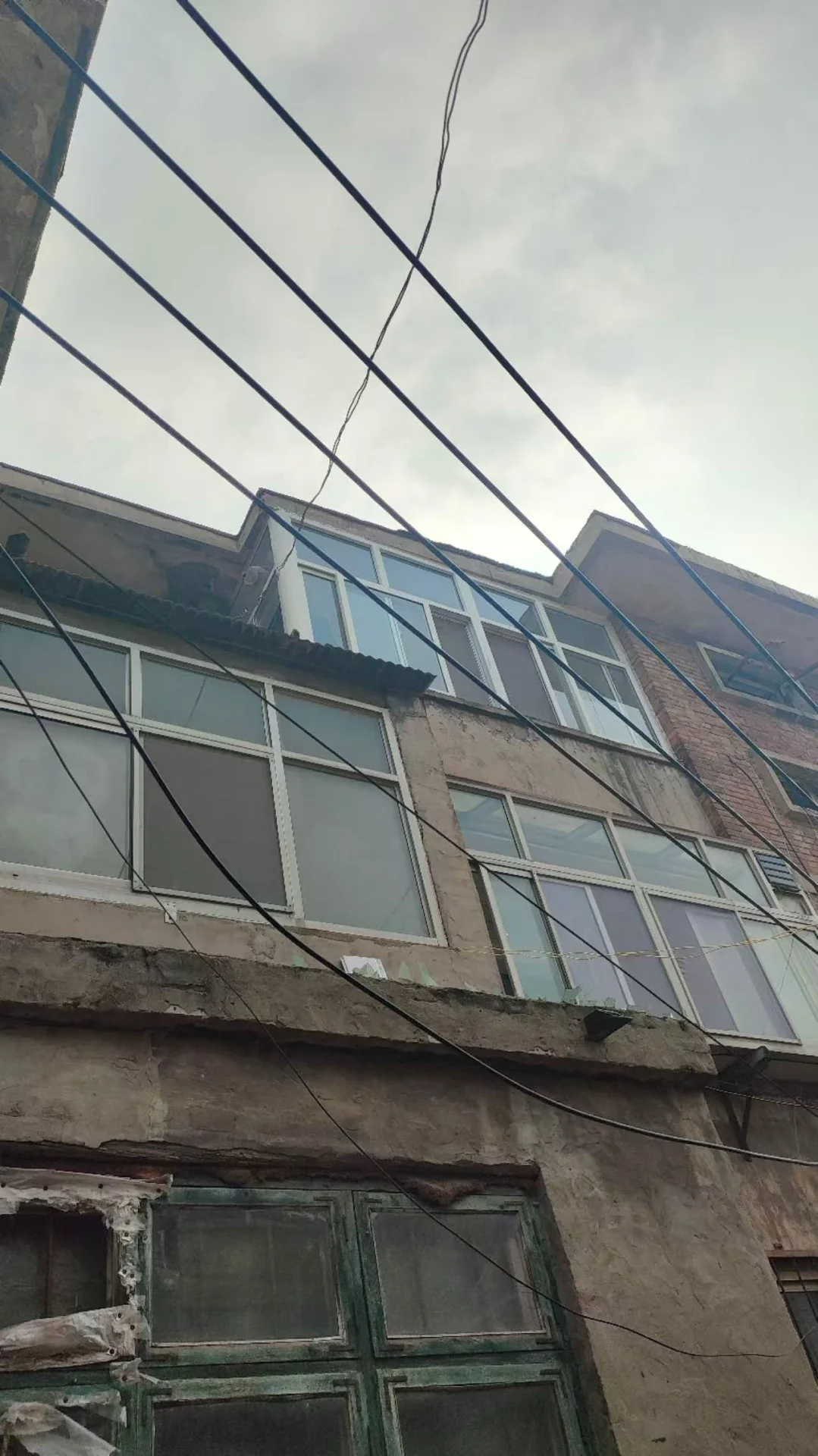 一栋多层住宅建筑的立面，外墙呈浅色调，窗户分布均匀，上方有密集的电线穿过视野。整体风格较为朴素实用，展现了城市居住环境的日常景象。