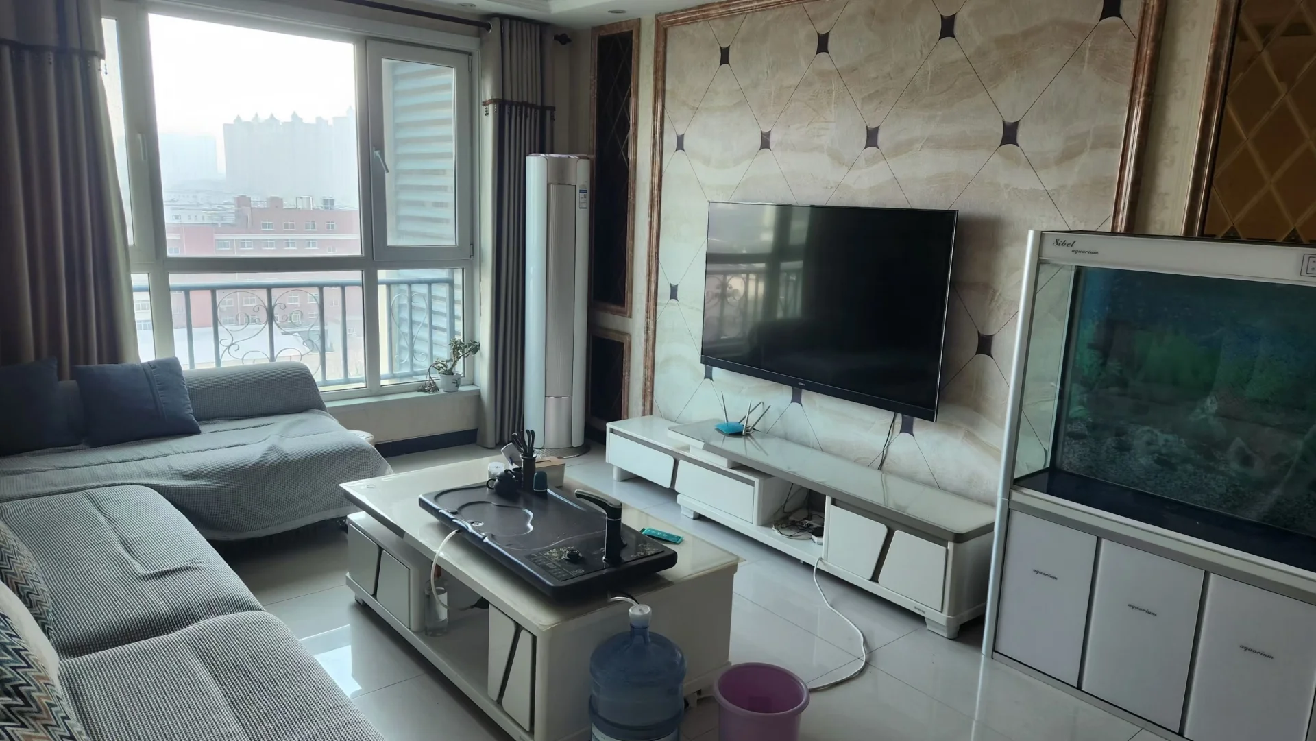 客厅场景，墙面装饰有几何图案，配有大型沙发和电视墙。采光良好，整体装修风格偏向现代简约，空间布局开阔。