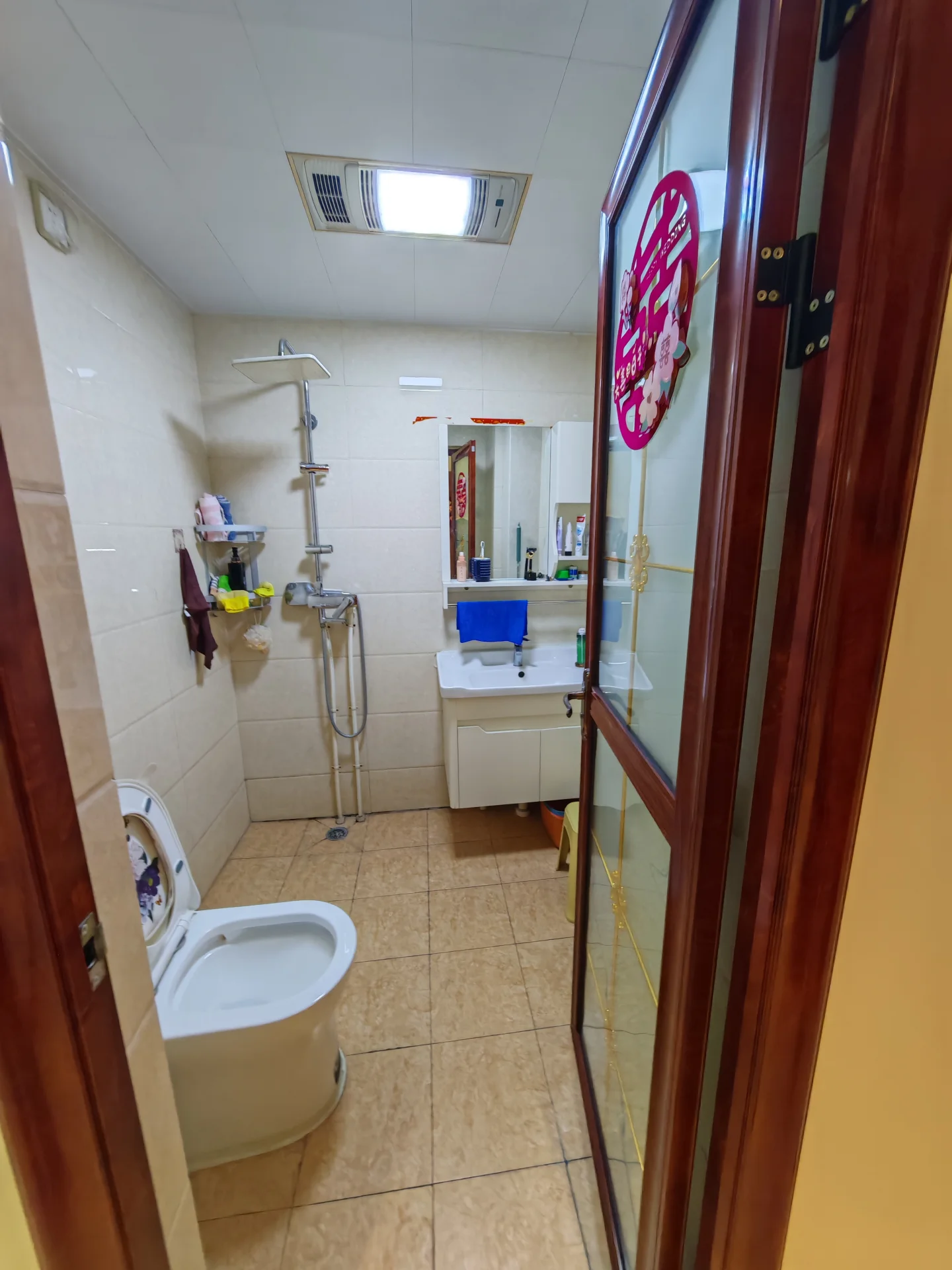 卫生间空间，墙面和地面铺设浅色瓷砖，配置有马桶、淋浴区和洗手台。整体装修风格基础实用，光线适中。