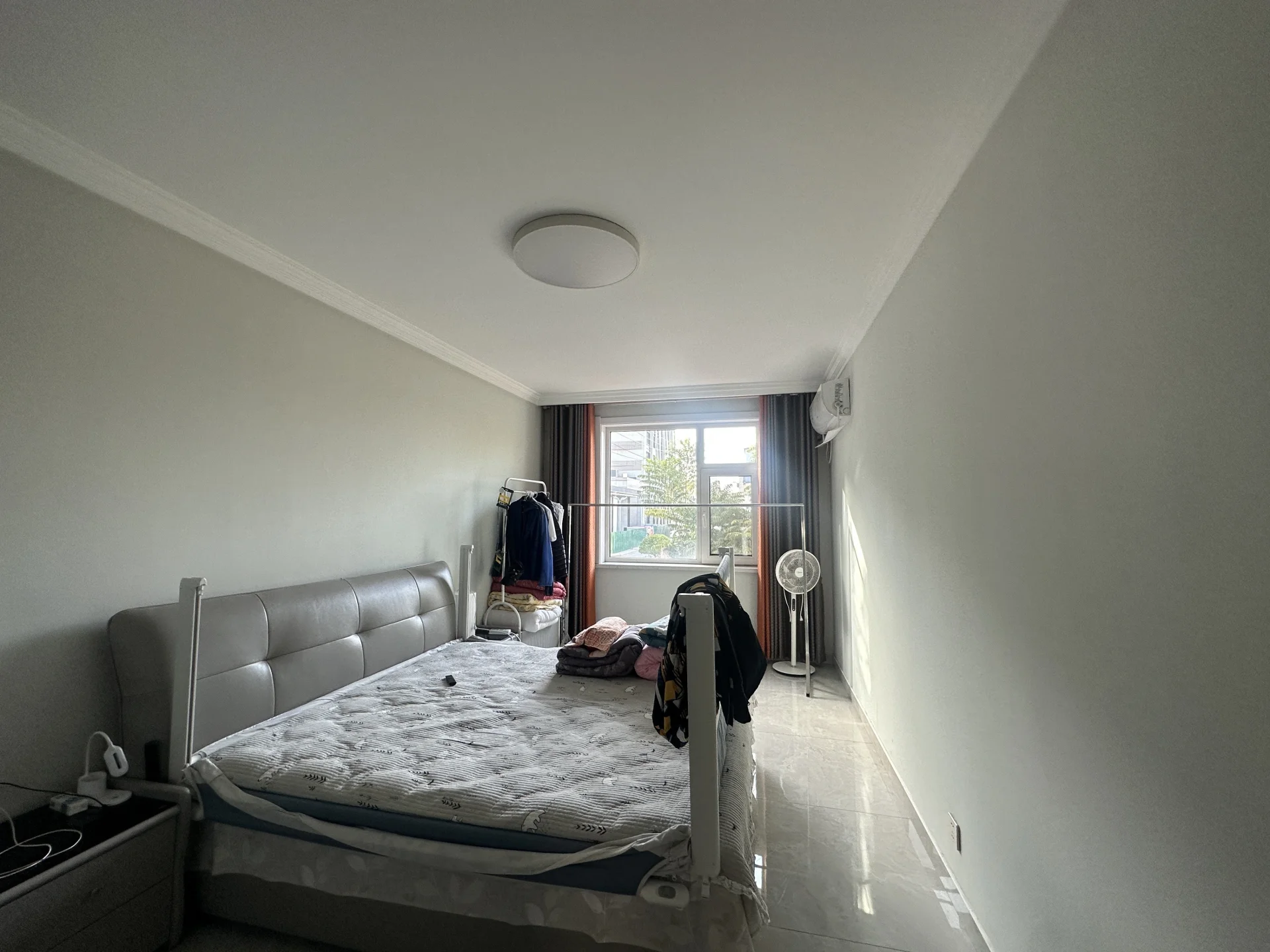 卧室空间，床头采用米色软包设计，房间整体装修风格偏现代简约。采光良好，天花板上安装有圆形吸顶灯，环境整洁舒适。