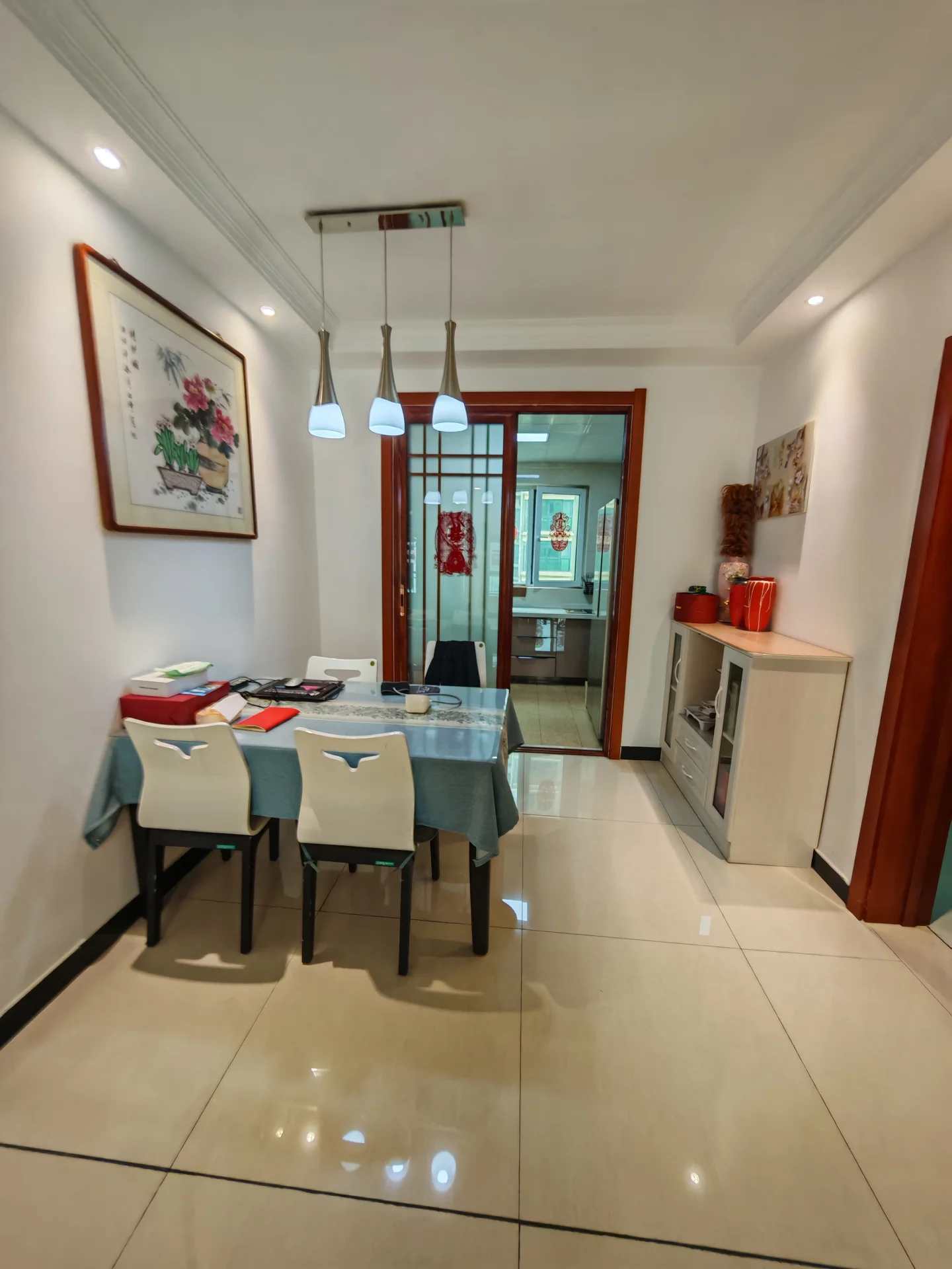 餐厅空间，铺设浅色大理石纹地砖，配有深色餐桌和几把白色靠背椅。天花板上悬挂着多盏现代风格的吊灯，整体环境简洁明亮。
