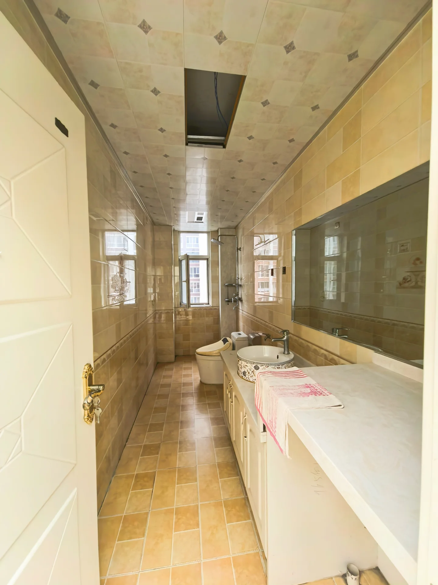 卫生间空间，墙面和地面铺设米色调瓷砖，设计简洁实用。空间布局清晰，配有洗手台、马桶及淋浴区域，光线适中，整体风格偏向基础功能型装修。