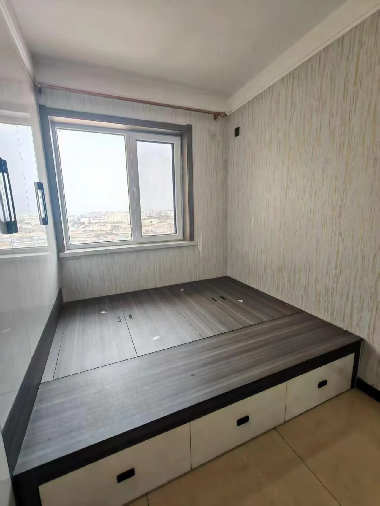 卧室空间，采用深色木纹风格的床头柜/储物柜作为主要家具，搭配简洁的墙面和充足的自然采光。整体装修风格偏向现代简约，环境整洁。