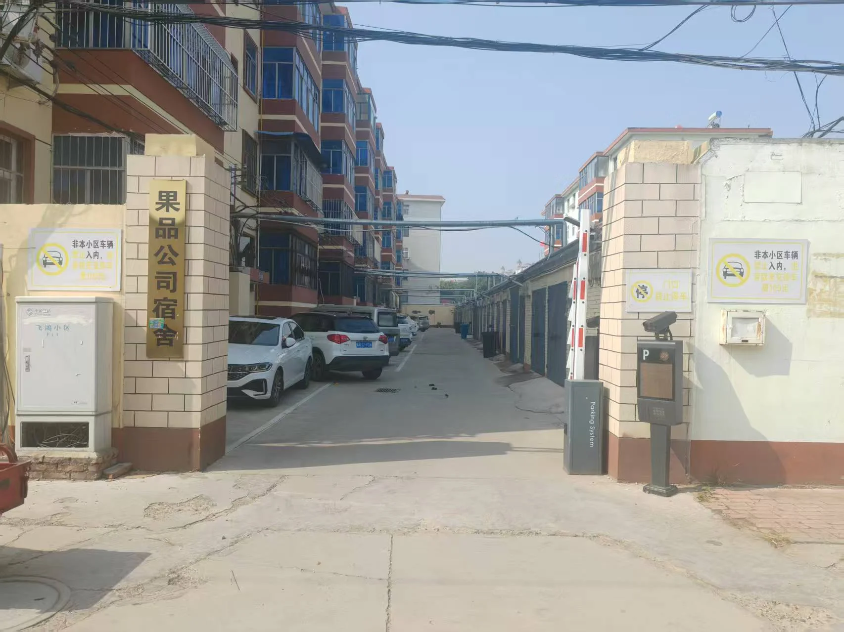 一处住宅小区入口场景，两侧有带有标识的门岗建筑，中间是通往小区内部的道路，背景可见多栋现代风格的居民楼。
