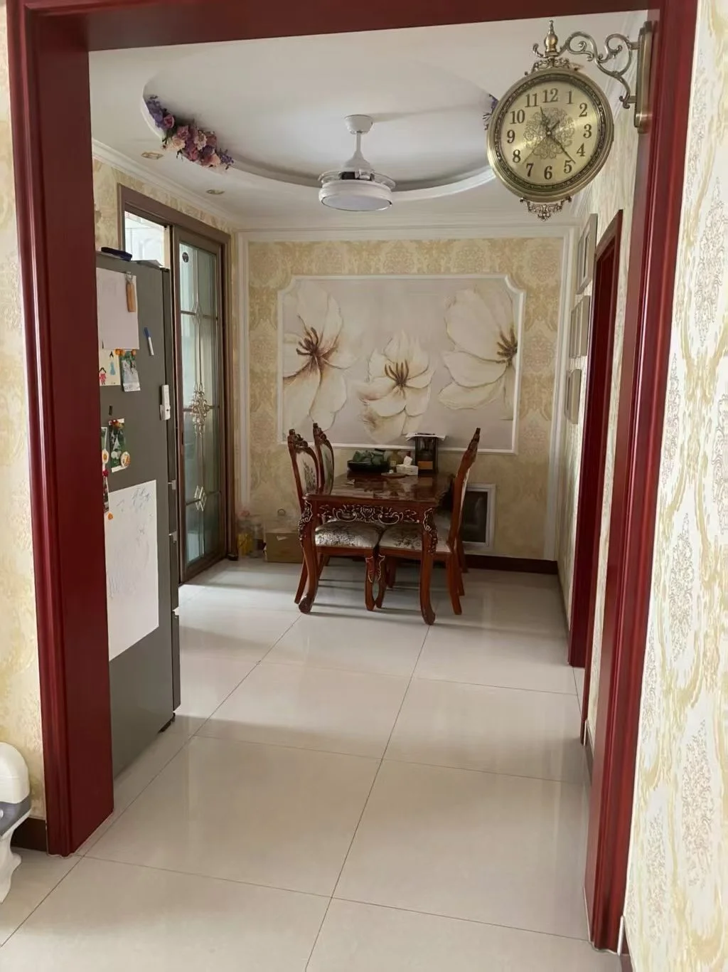 餐厅空间，墙面装饰有大型白色花卉图案，配有一套深色木质餐桌椅。天花板上安装了吊灯，整体环境光线适中，风格偏向古典或温馨的家居风格。