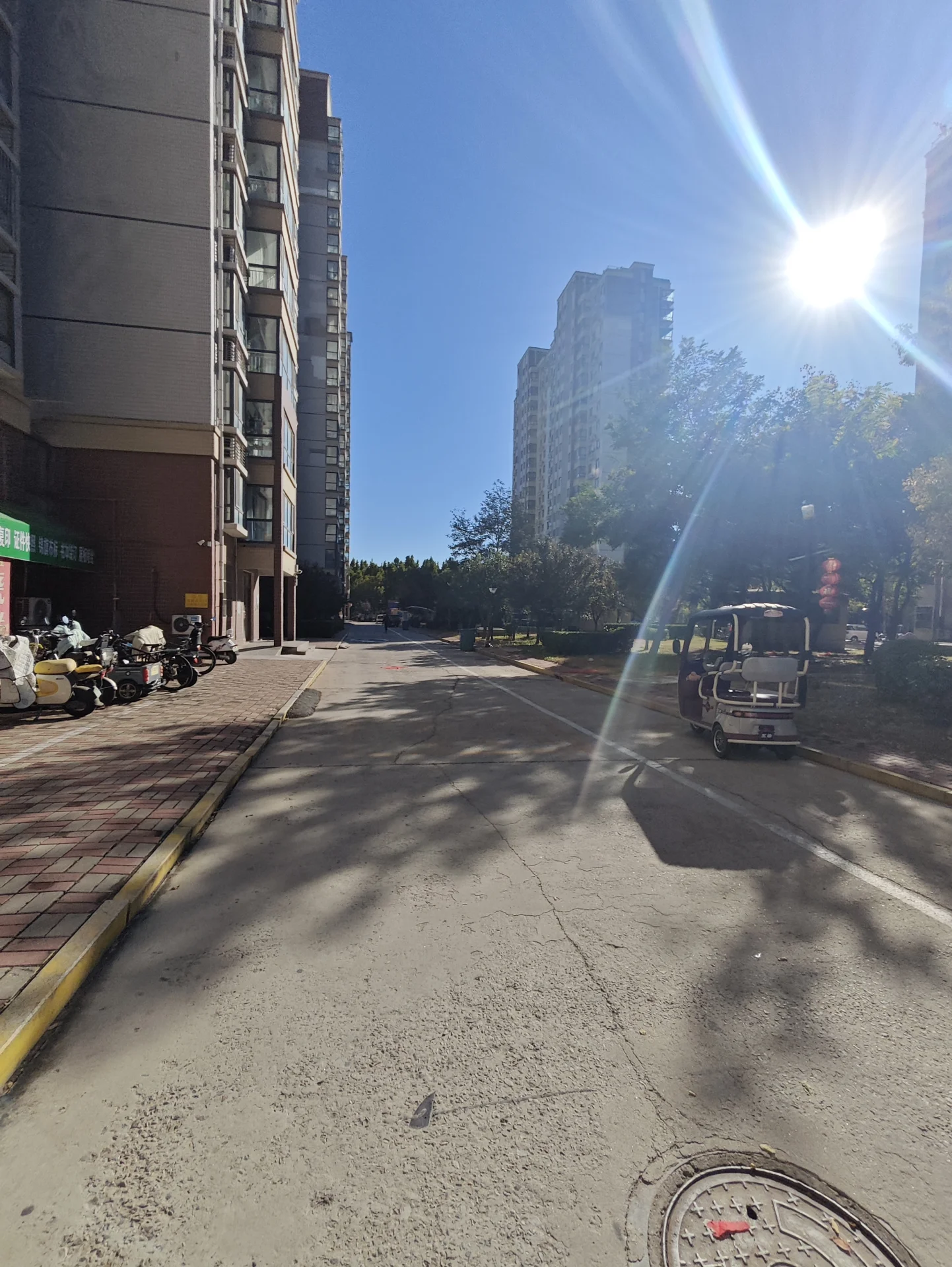 一条城市街道，两侧是高层住宅建筑，街道中央有车辆行驶，阳光充足，整体呈现现代城市居住环境的氛围。