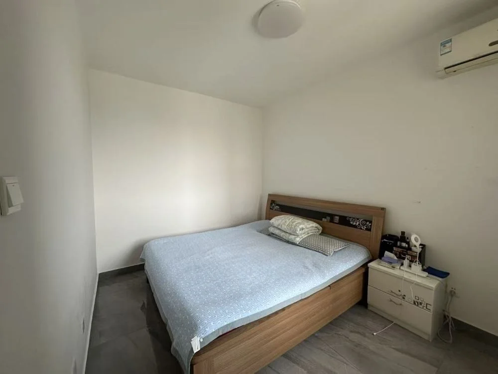 卧室空间，采用木质床架和浅色地板，墙面简洁，配有空调和电视等基础家电。采光适中，整体呈现基础、实用型的装修风格。