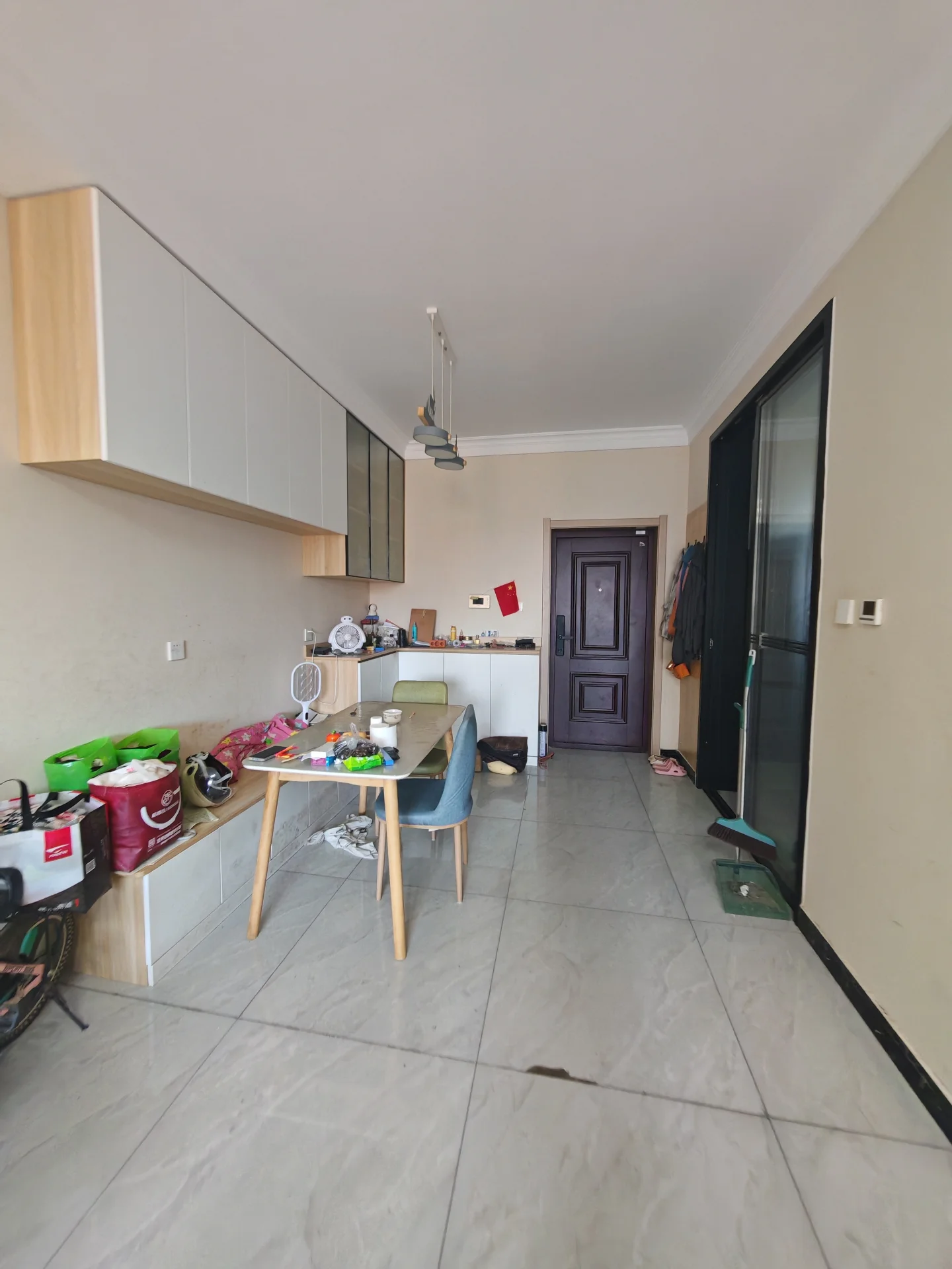 厨房和餐厅区域的组合空间，橱柜采用浅色木纹设计，配有餐桌和椅子。地面铺设大尺寸浅色瓷砖，整体光线充足，装修风格偏向实用简约。