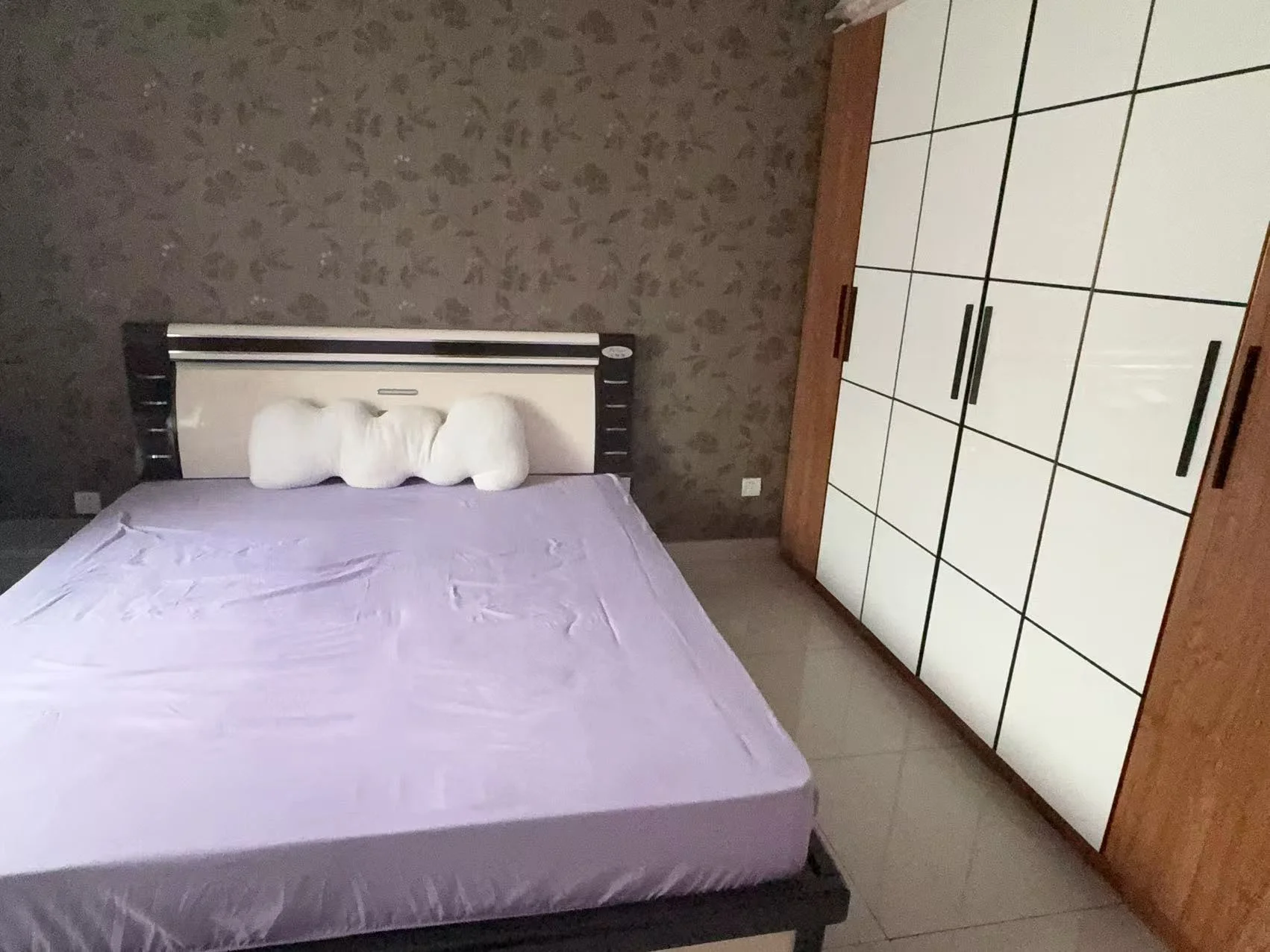 卧室空间，床铺为深色框架，搭配白色床品，背景墙采用带有纹理的灰绿色壁纸。房间光线适中，整体环境简洁实用。
