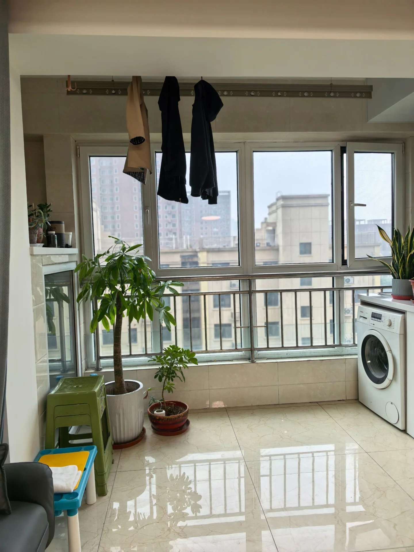 阳台空间，地面铺设浅色瓷砖，配有大型盆栽绿植和洗衣机等家电。视野开阔，采光良好，整体环境简洁实用。