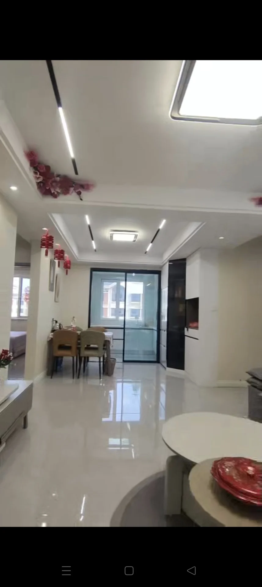 这是一个开放式居住空间，包含餐厅和客厅区域。地面为大尺寸浅色瓷砖，天花板安装了嵌入式灯带照明，整体装修风格偏向现代简约。空间布局开阔，采光良好。