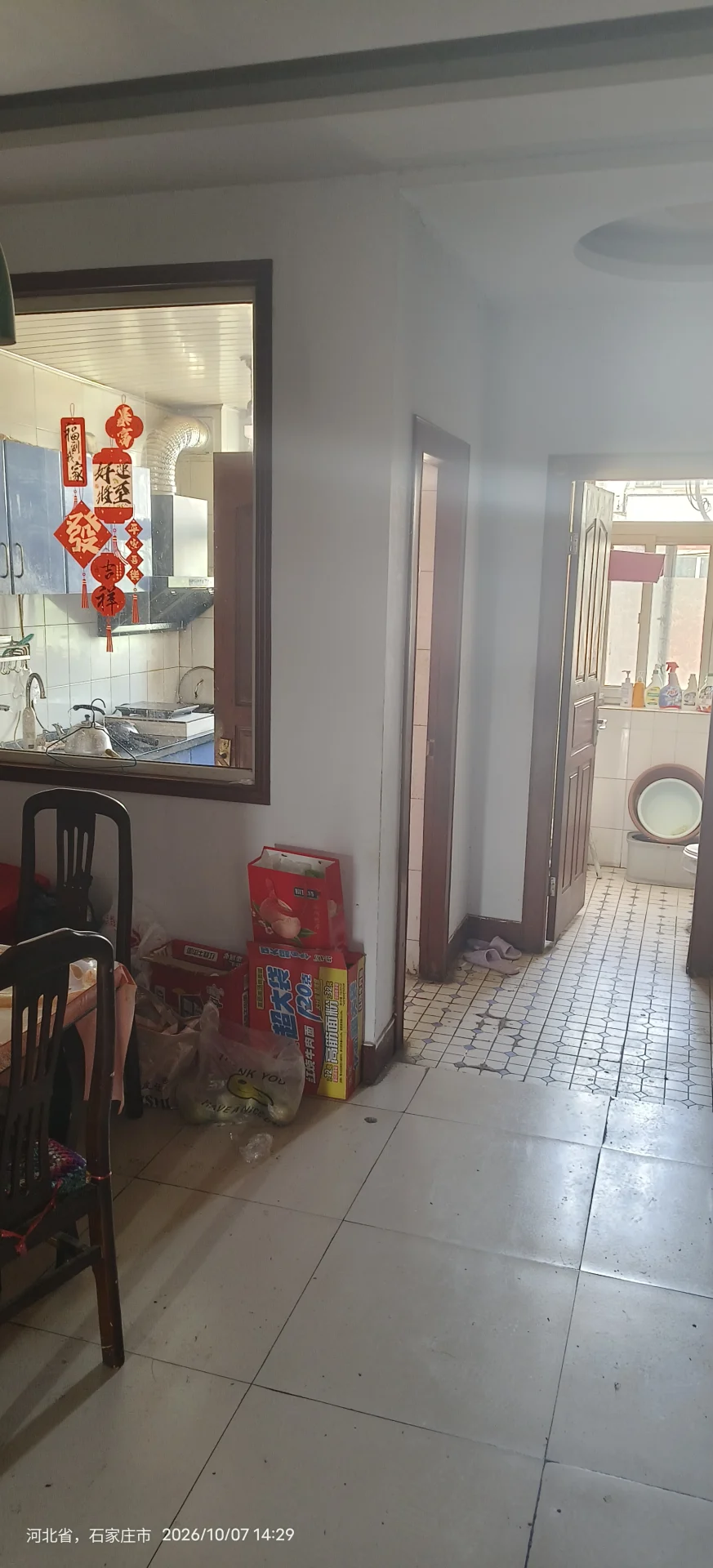 这是一个室内空间，地面铺设浅色瓷砖，墙面简洁，整体装修风格偏基础实用型。空间内可见厨房区域和部分储物物品，采光适中。