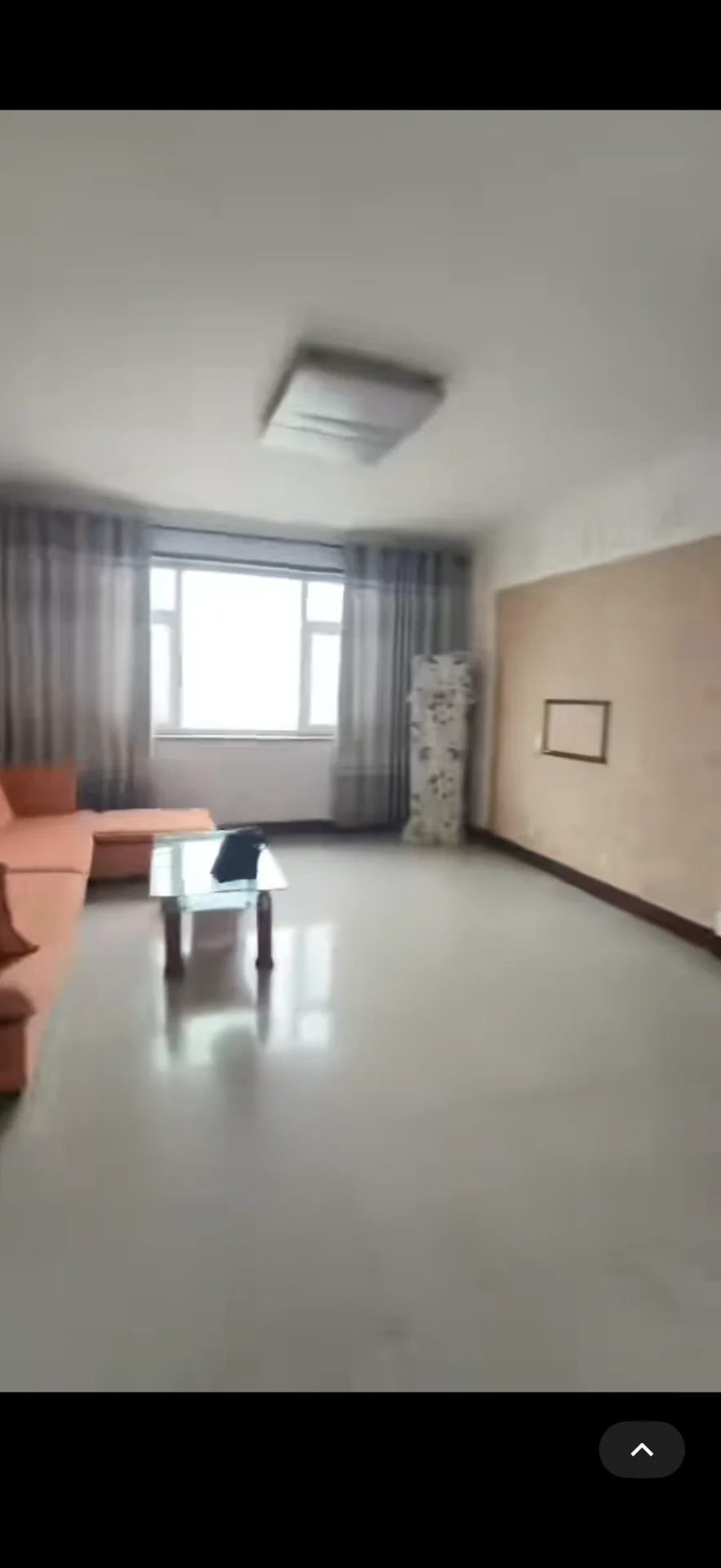 客厅空间，地面为抛光水泥材质，墙面采用浅色调涂料，配有橙色布艺沙发和玻璃茶几。采光良好，整体呈现基础装修状态。