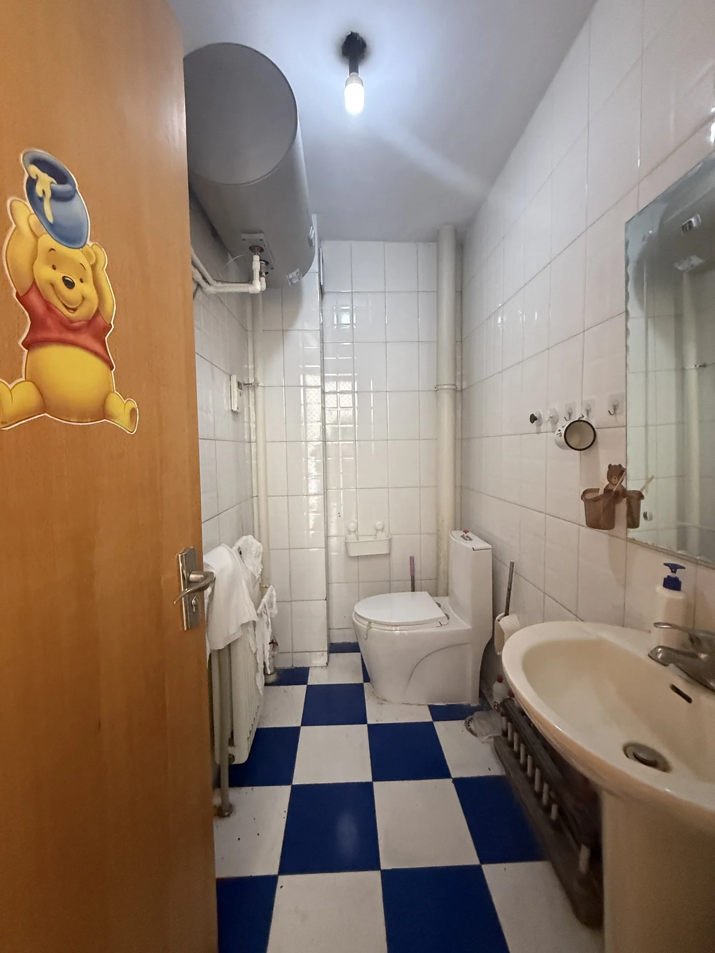 卫生间空间，墙面采用白色瓷砖铺设，地面采用黑白相间的方格瓷砖设计。空间布局简洁实用，光线适中，具备基础的卫浴设施。