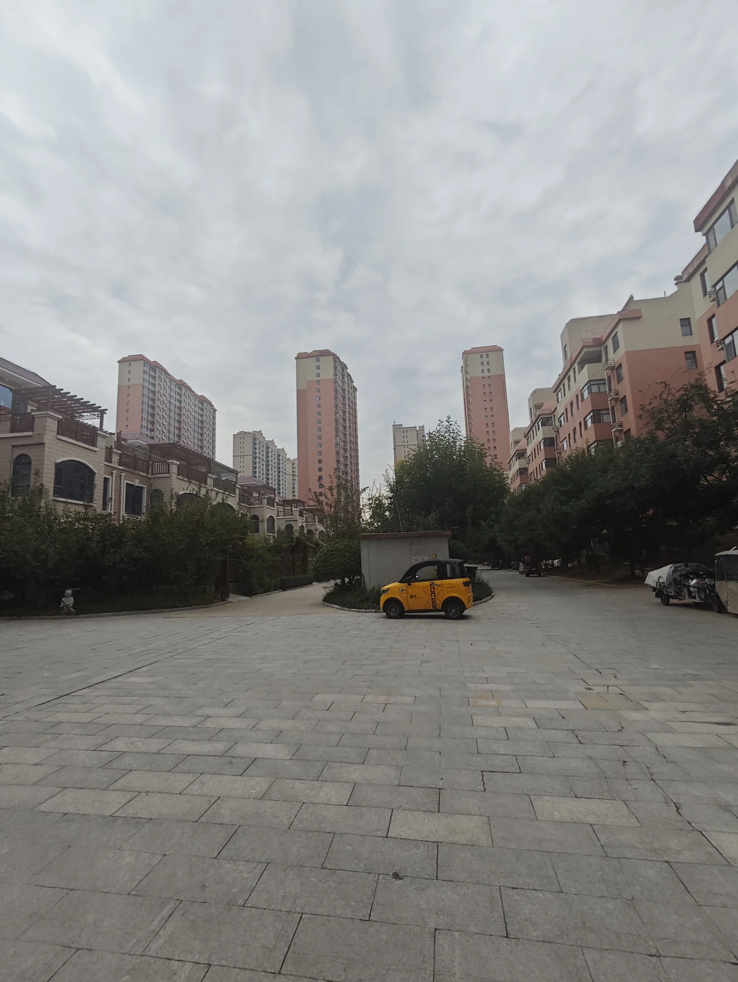一处城市住宅区内部的空旷广场，背景是多栋高层现代风格的住宅楼，周围有绿化带和停放的车辆，整体环境显得宽敞且具有一定的居住氛围。