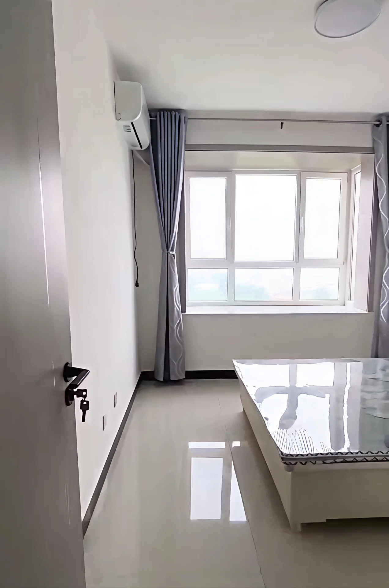 这是一个室内空间，地面为浅色瓷砖，墙面简洁，配有空调和窗户。房间内摆放着一张桌子，整体装修风格偏向基础和实用主义，采光良好。