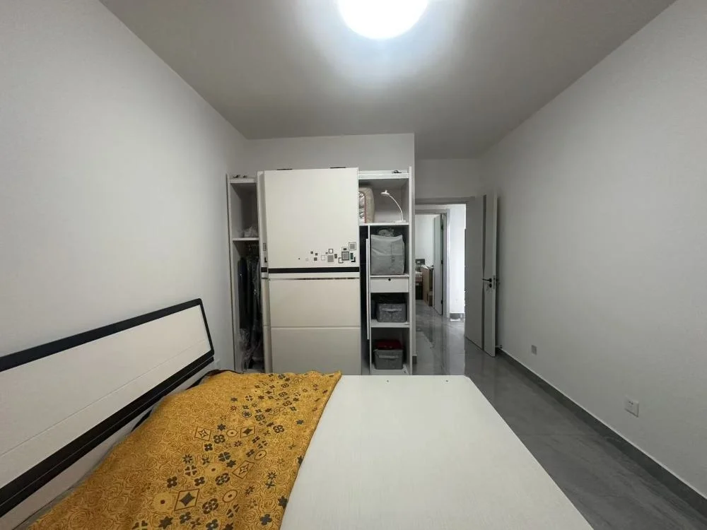 卧室空间，墙面为白色，地面铺设浅色瓷砖。房间内摆放有床和大型白色冰箱，整体装修风格简洁明快，采光良好。