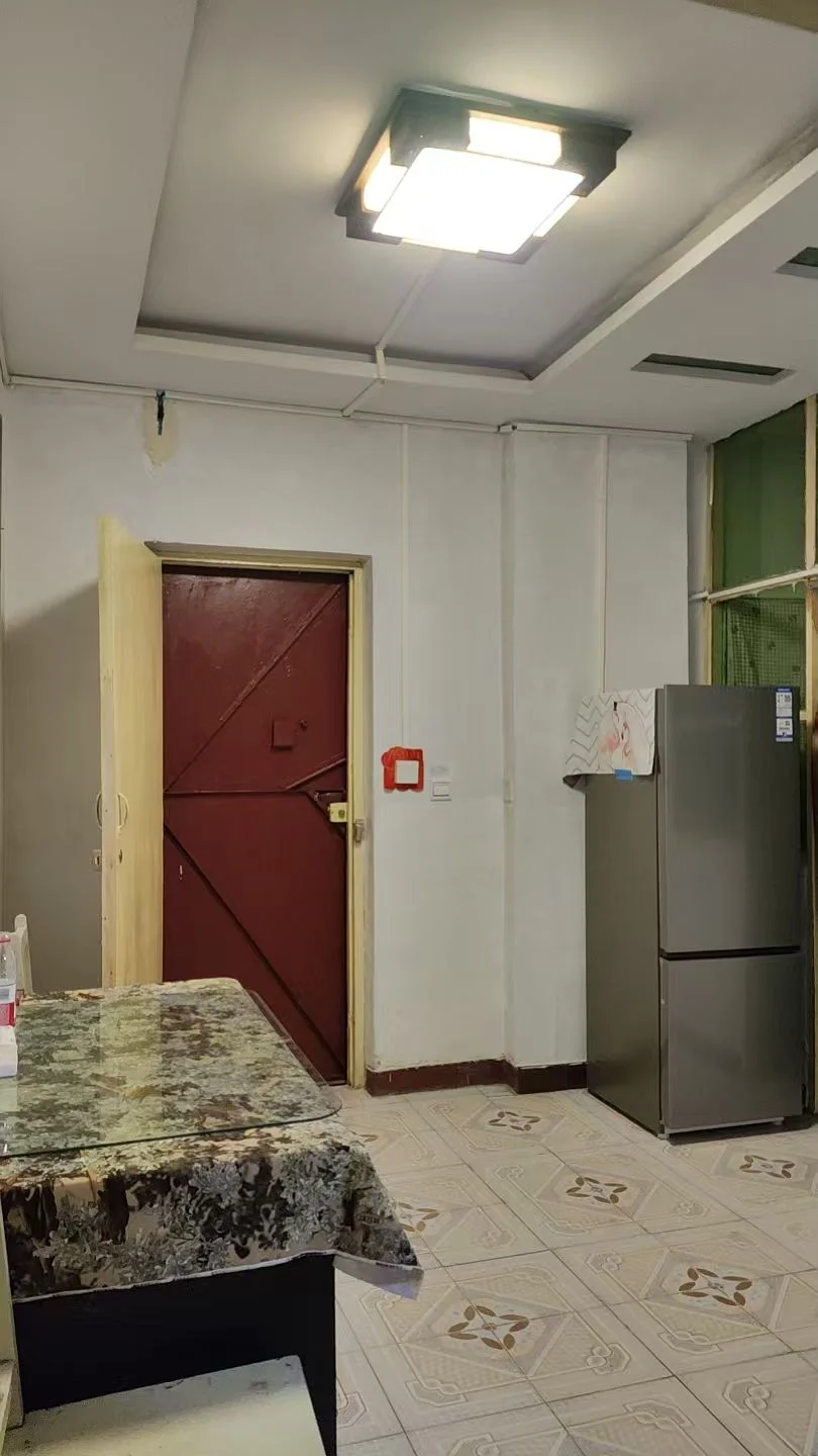 厨房区域，配有深色台面和不锈钢大型冰箱。空间光线充足，整体呈现基础的居住环境。