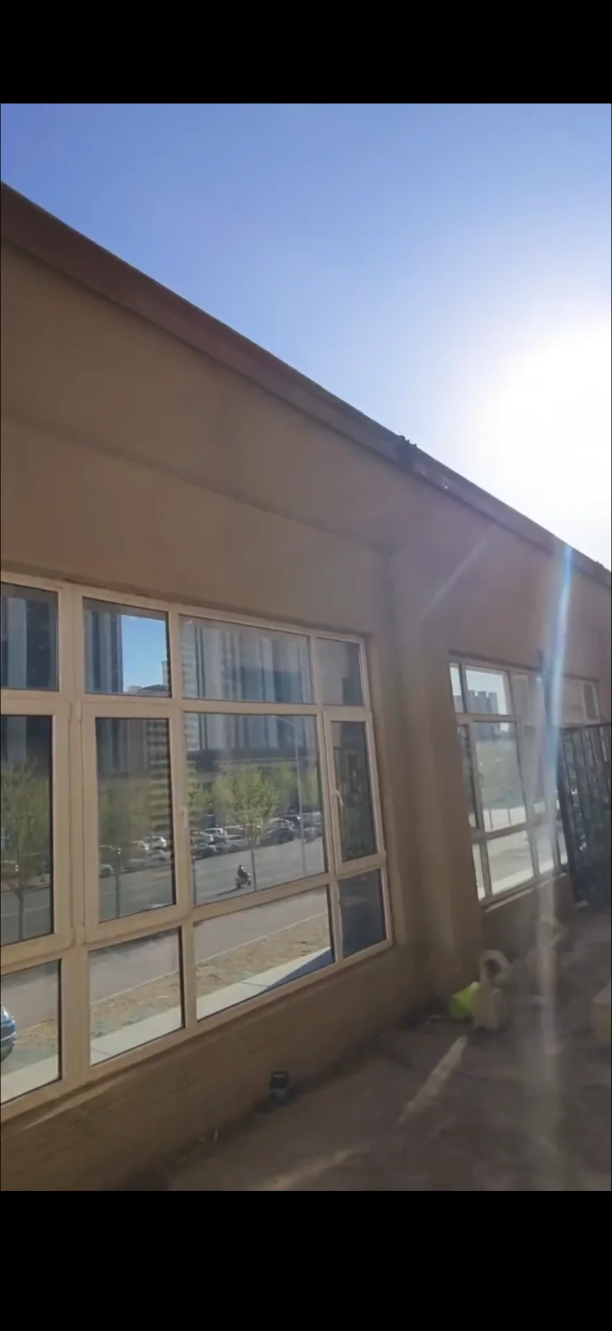 一栋低层商业建筑的外观，外墙呈浅米色，设有大面积的落地窗，展现出现代简约的商业风格。建筑前方有少量停放的车辆和绿化带，整体环境开阔明亮。