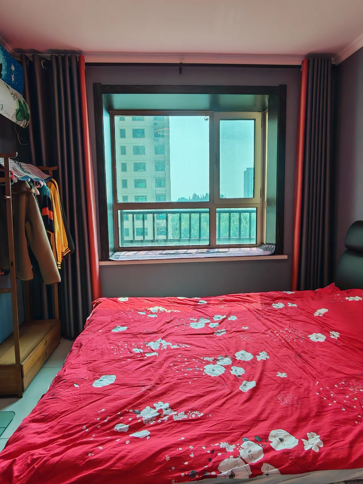 卧室场景，床铺铺设着红底白花的被褥，房间内有衣柜和窗户。采光适中，整体呈现基础的居住环境。